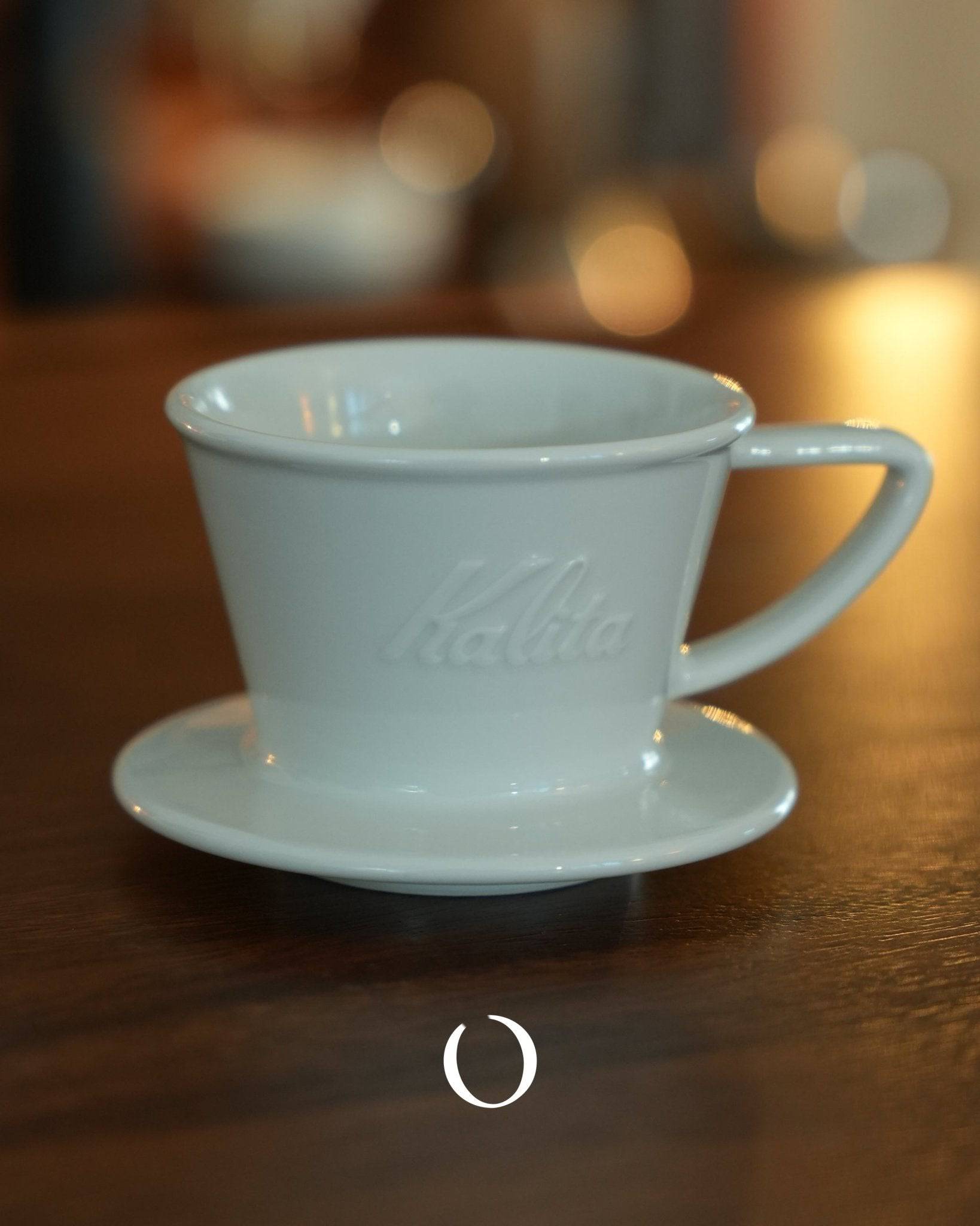 KALITA & HASAMI ceramic coffee dripper, white porcelain cup with saucer, embossed Kalita logo, on wooden surface with soft background bokeh, traditional Japanese Hasami-yaki craftsmanship