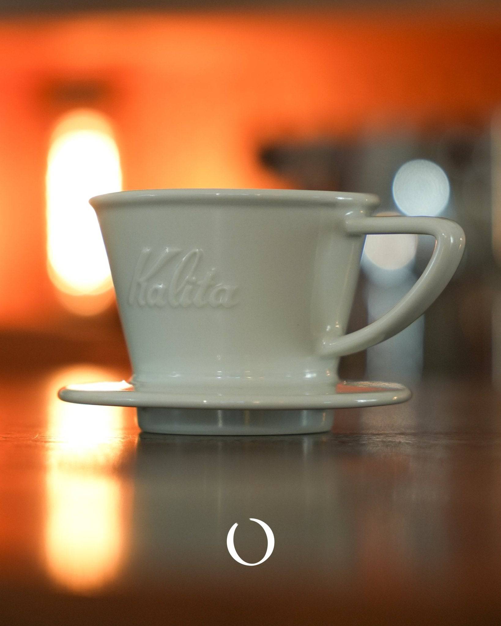 KALITA ceramic coffee dripper on a reflective surface with warm orange background lighting, showcasing Japanese craftsmanship and design for premium coffee brewing