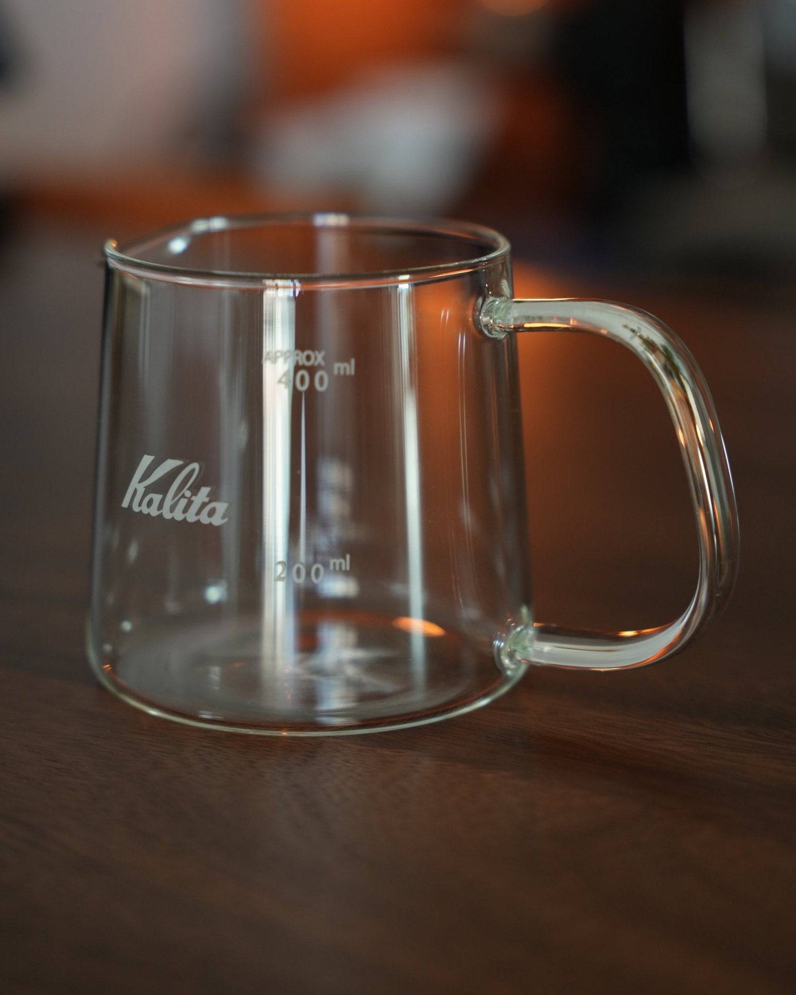 Kalita JUG400 heat-resistant glass coffee jug with 400ml capacity, featuring clear volume markings, ergonomic handle, and brand logo on a wooden surface