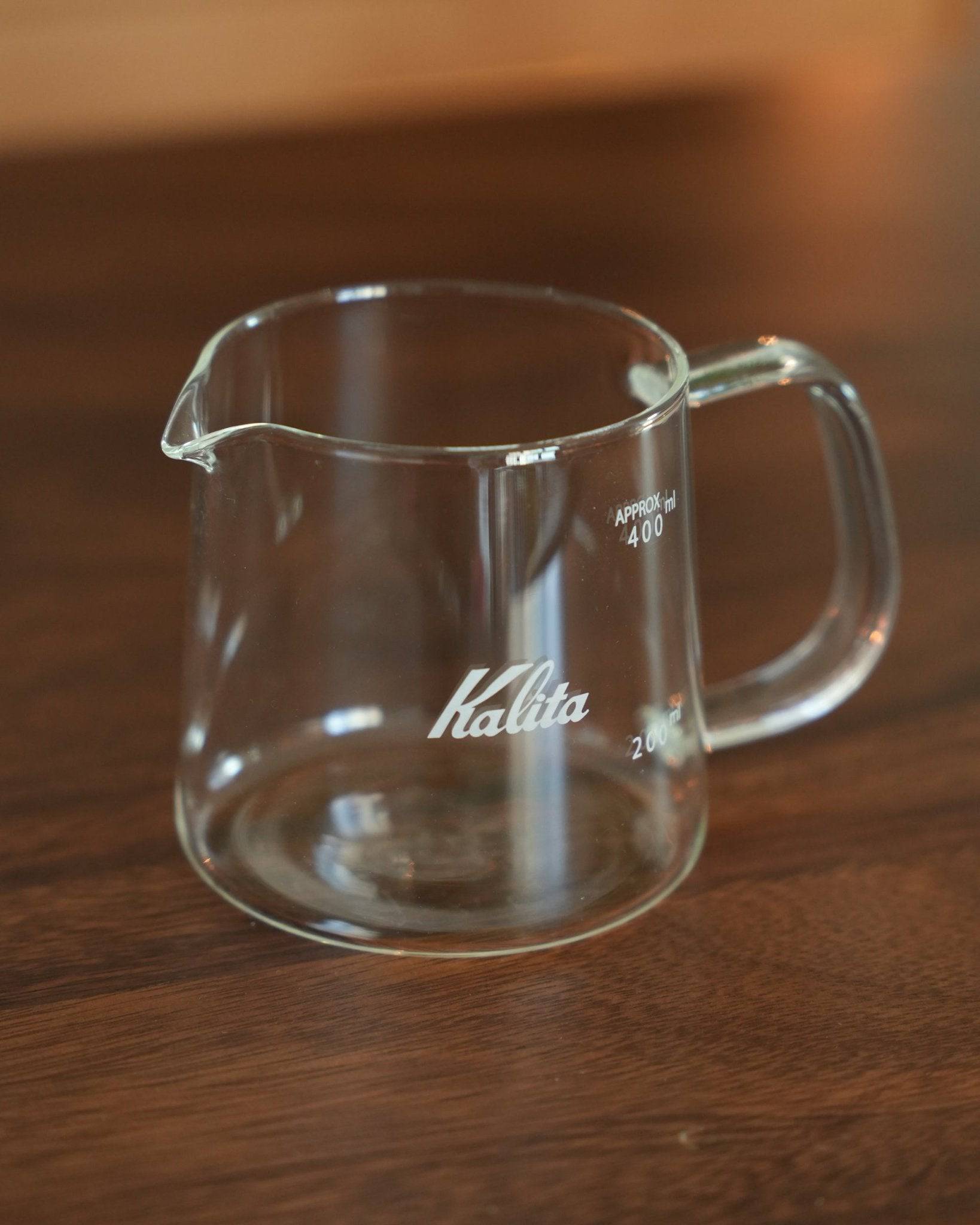 Kalita JUG400 glass coffee server on wooden surface, 400ml capacity, clear heat-resistant design with pouring spout, comfortable handle, and visible measurement markings, showcasing elegant simplicity and functionality for pour-over brewing
