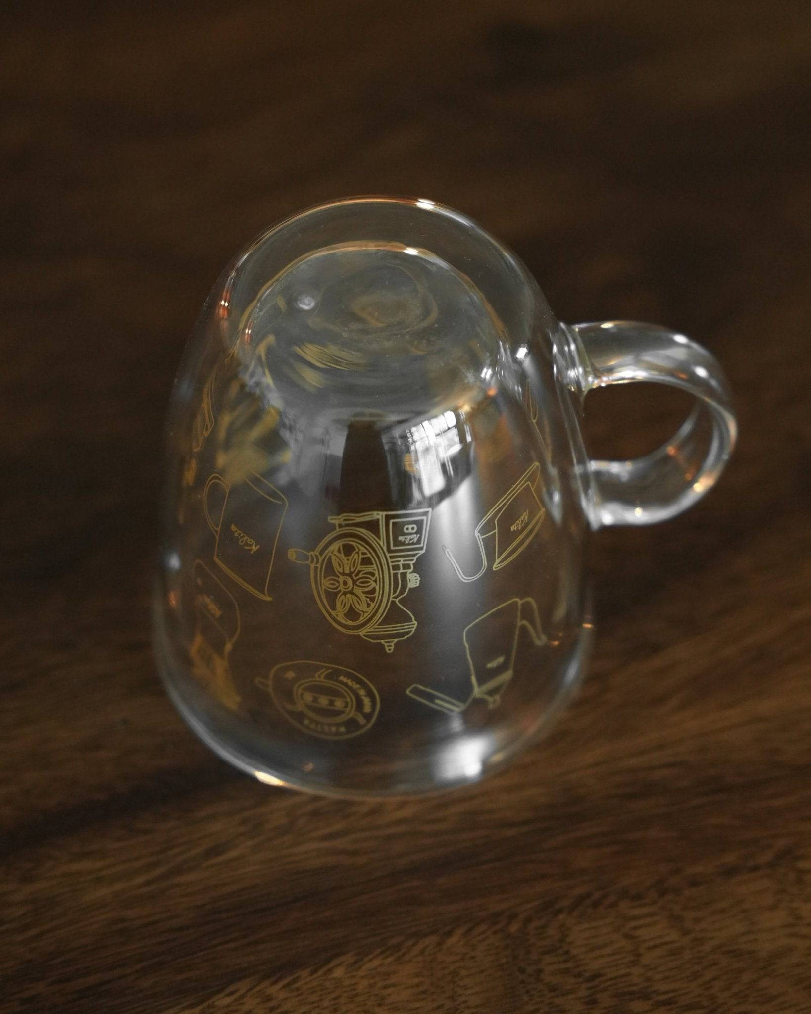 Kalita double-walled glass mug with coffee-themed etching, featuring grinder and filter illustrations, on wooden surface