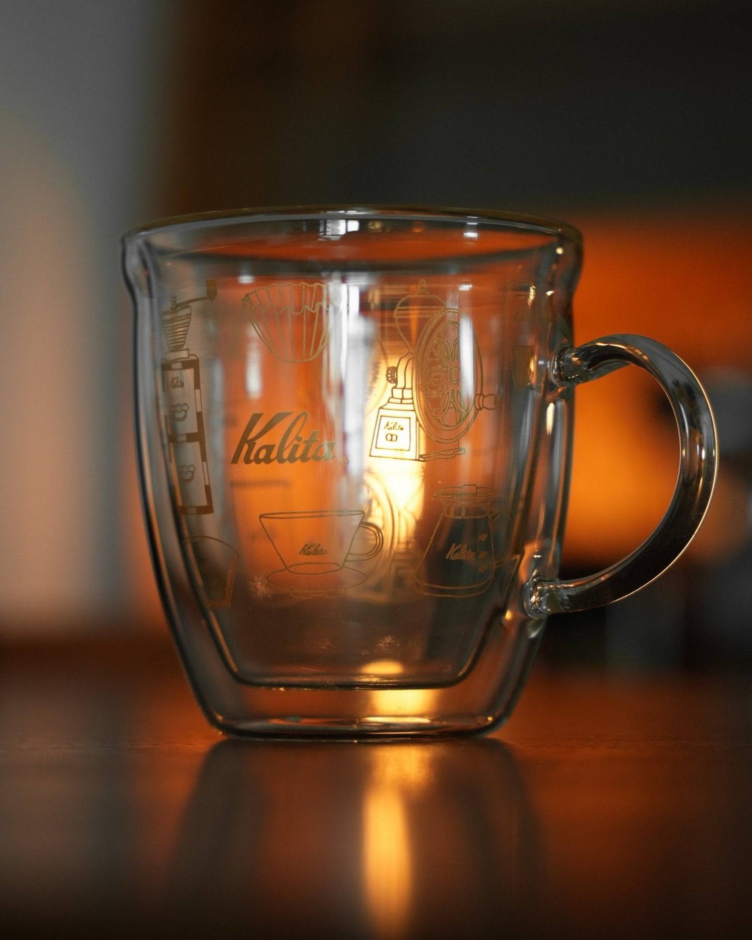 Kalita double-walled glass mug with coffee equipment etching, illuminated by warm light, showcasing its transparent design and brand logo