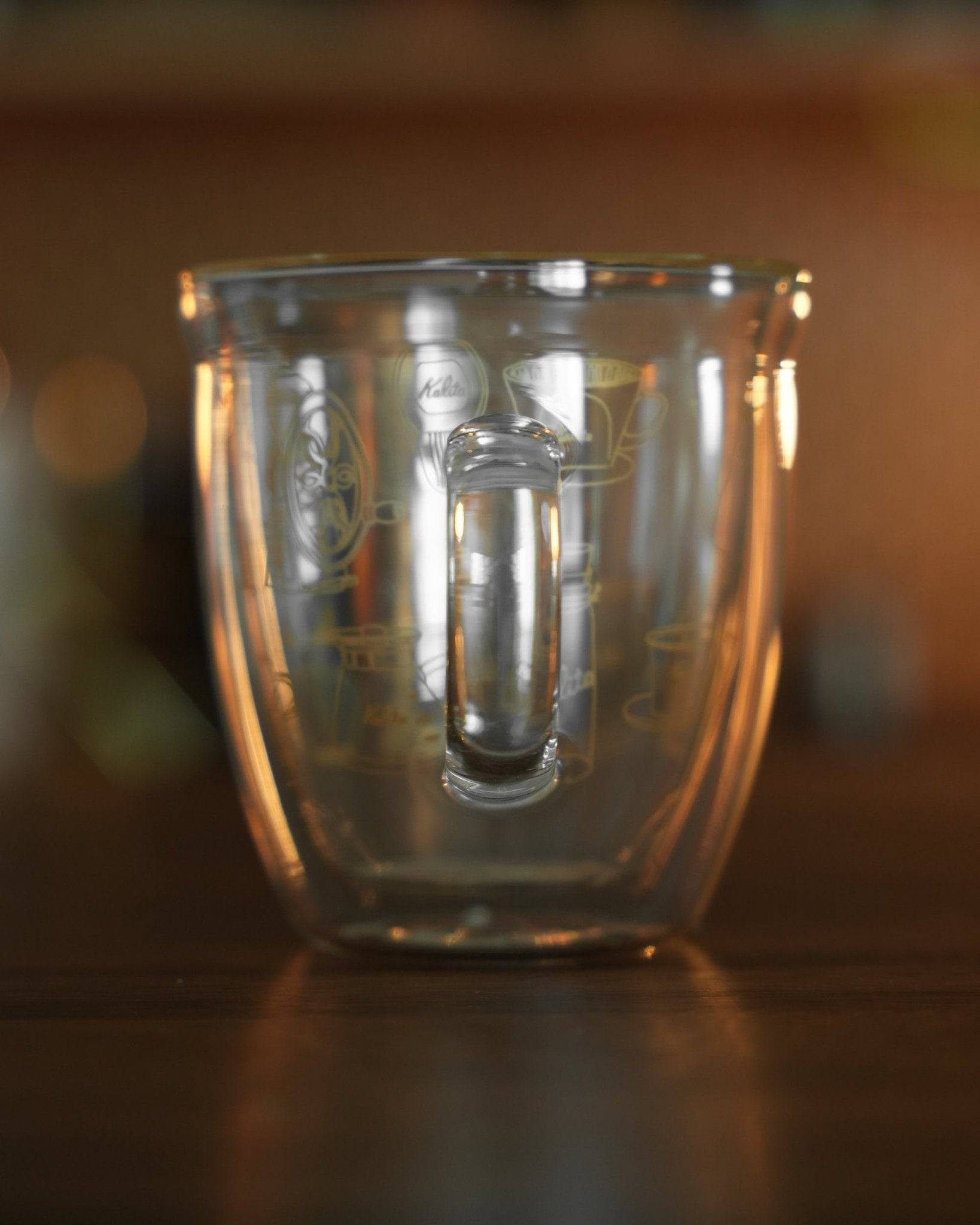 Kalita double-walled glass mug with coffee grinder and filter design, showcasing transparency and elegant craftsmanship on wooden surface with warm lighting
