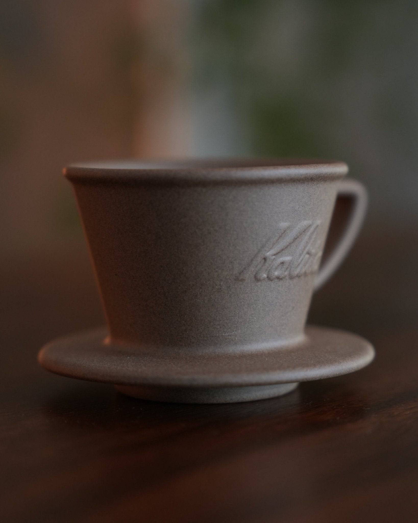 Kalita SG-155 Hasami-yaki sandstone coffee dripper on wooden surface, showcasing its rustic texture and elegant design with Kalita logo embossed on side, perfect for artisanal coffee brewing