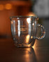 Kalita double-walled glass mug with etched coffee cup design, illuminated by warm ambient light, showcasing transparency and craftsmanship