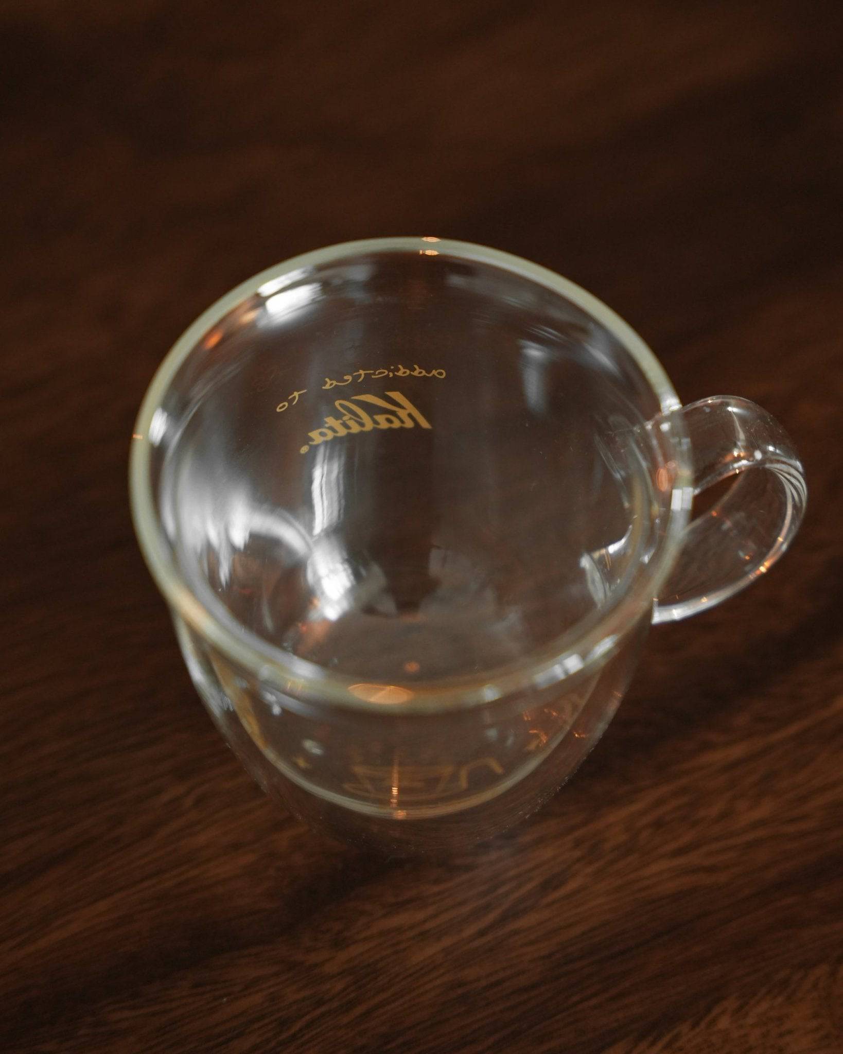 Kalita double-walled glass mug on wooden surface, showcasing transparent design with gold Kalita logo and coffee grinder illustration