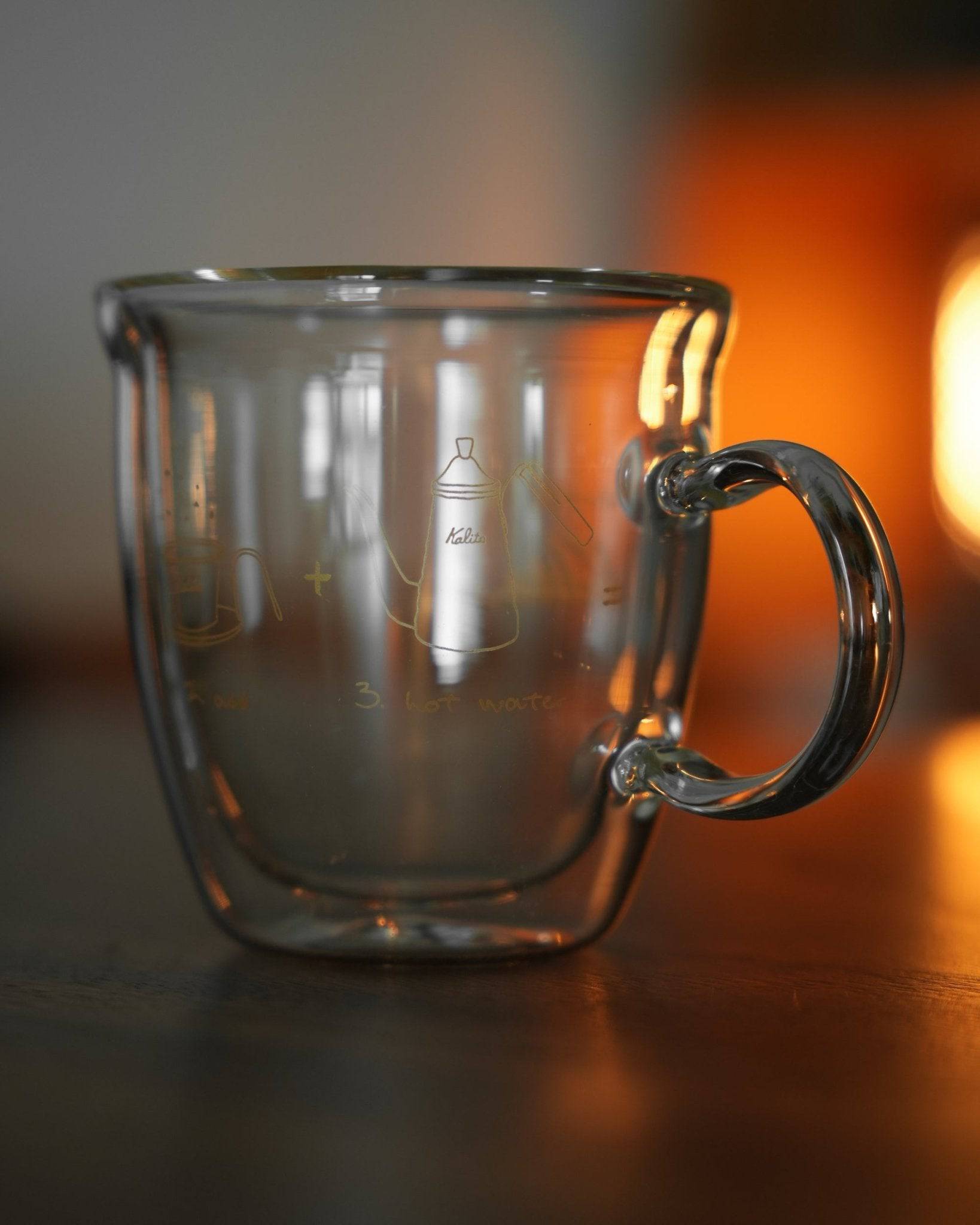 Kalita double-walled glass mug with coffee grinder and filter design, transparent 240ml cup on wooden surface with warm background lighting