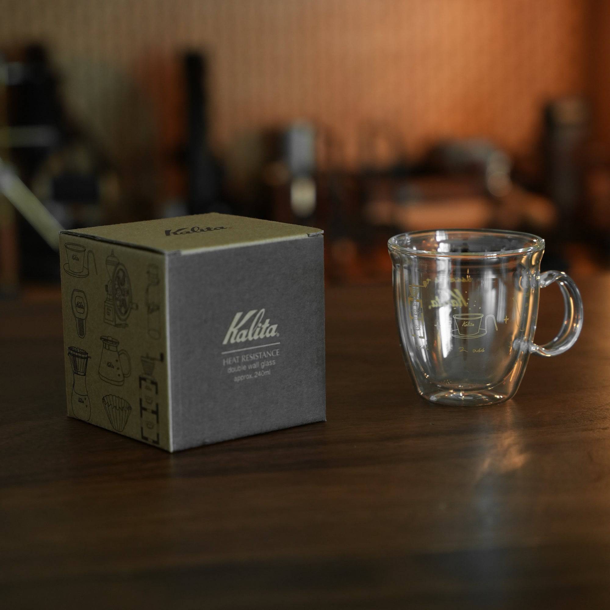 Kalita double-walled glass mug with product box on wooden table, coffee equipment in background, showcasing transparent design and brand packaging for SG 240ml cup