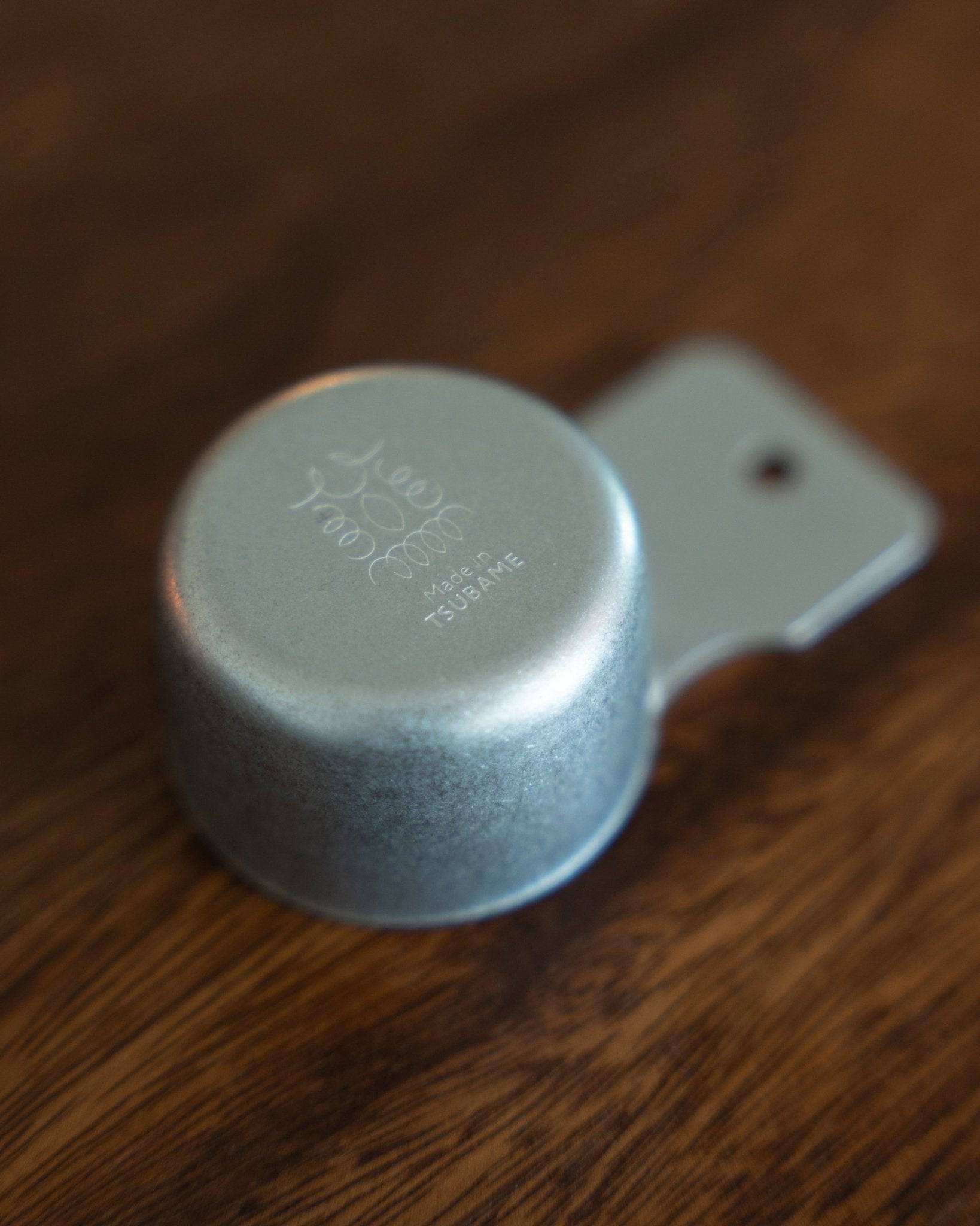 Kalita & Tsubame stainless steel coffee scoop, 10g capacity, matte finish, with engraved logo on wooden surface