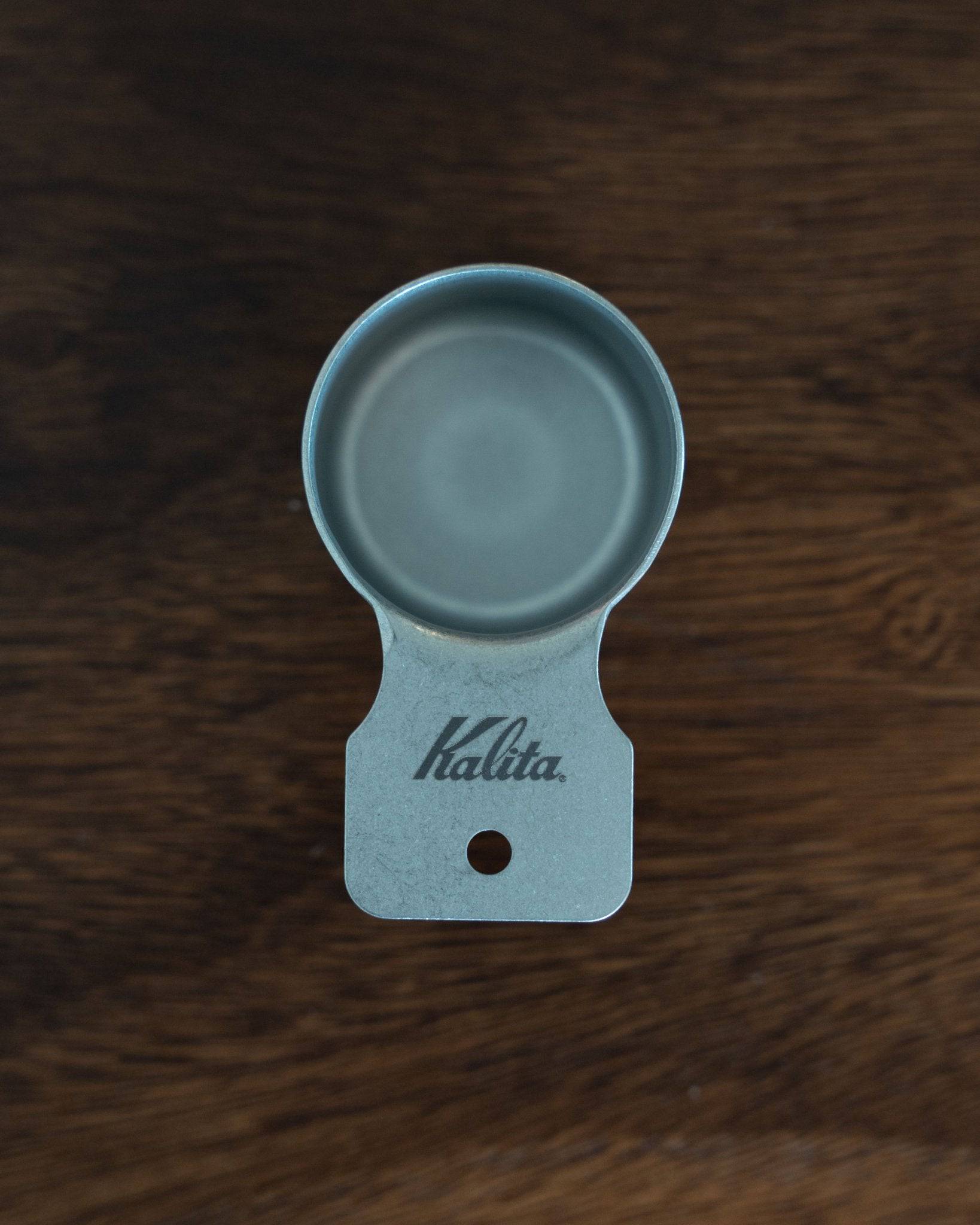 Kalita stainless steel coffee scoop, 10g capacity, S size, matte finish, circular bowl with flat handle, Kalita logo engraved, on dark wooden background