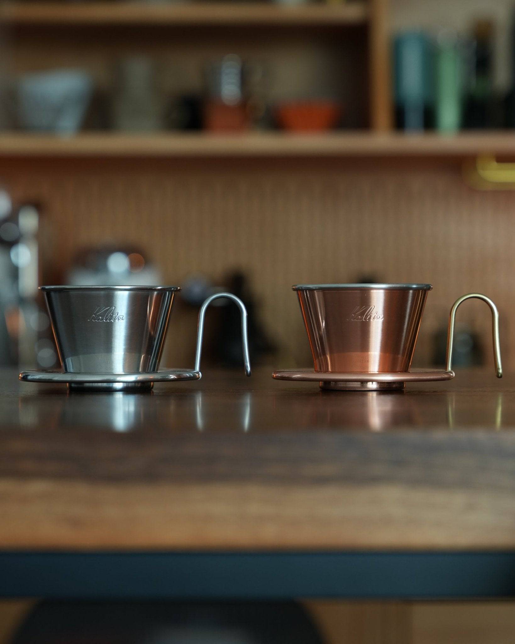 Kalita & TSUBAME WDC-155 copper and stainless steel pour-over coffee drippers side by side on wooden counter, showcasing premium craftsmanship and elegant design for specialty coffee brewing