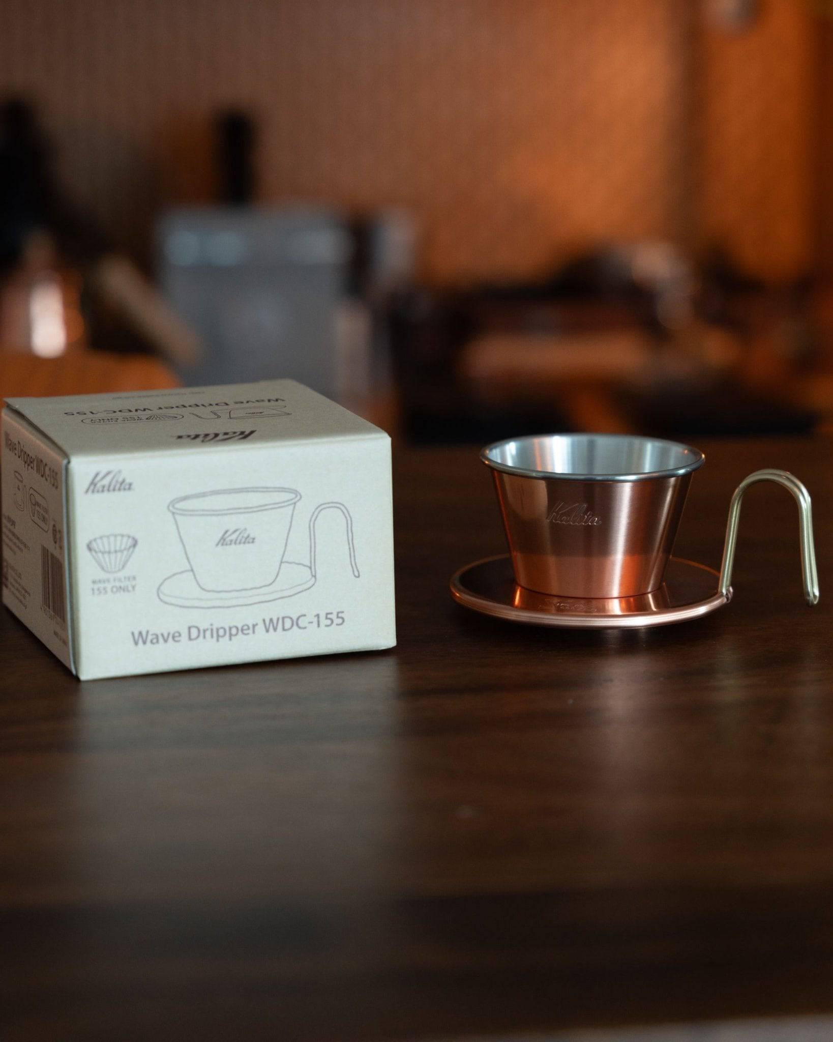 Kalita Wave Dripper WDC-155 copper coffee filter with product box on wooden table, showcasing elegant design and premium craftsmanship for pour-over brewing