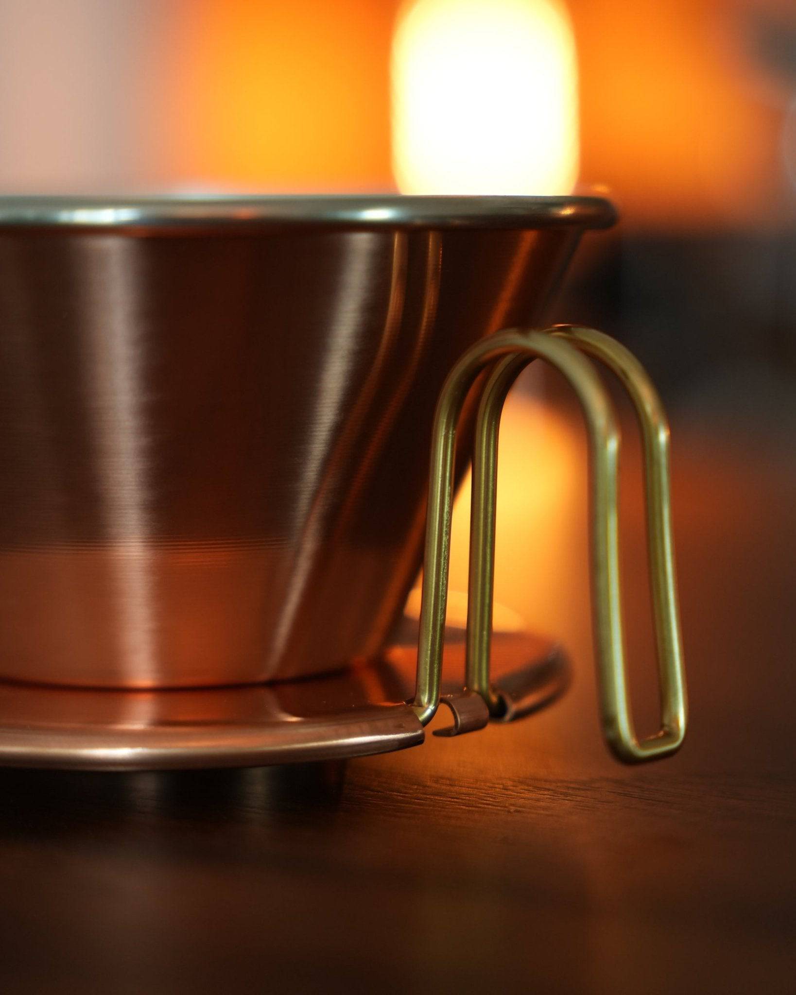 Kalita & TSUBAME WDC-185 copper pour-over coffee dripper with golden handle, showcasing its elegant design and premium craftsmanship in warm, ambient lighting on a wooden surface
