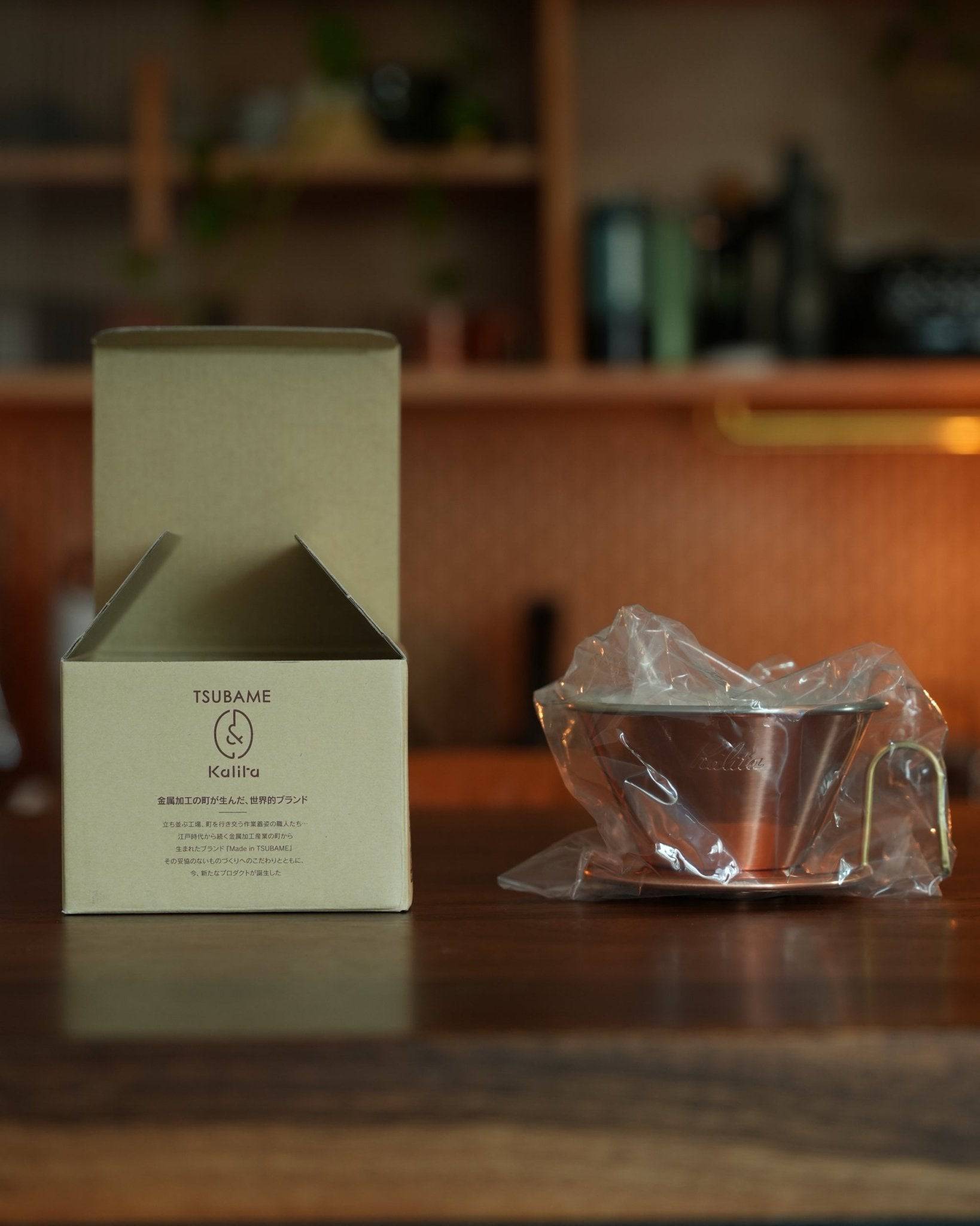 Kalita & TSUBAME WDC-185 copper coffee dripper with packaging box and wrapped product on wooden counter, showcasing premium Japanese craftsmanship for coffee enthusiasts