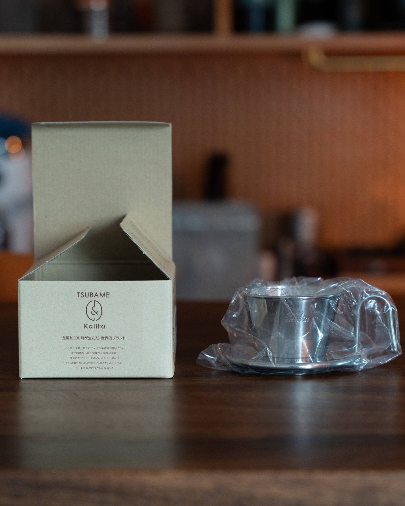 Kalita & TSUBAME WDS-155 stainless steel coffee dripper with packaging box and plastic-wrapped product on wooden counter, showcasing Japanese craftsmanship and premium coffee brewing equipment