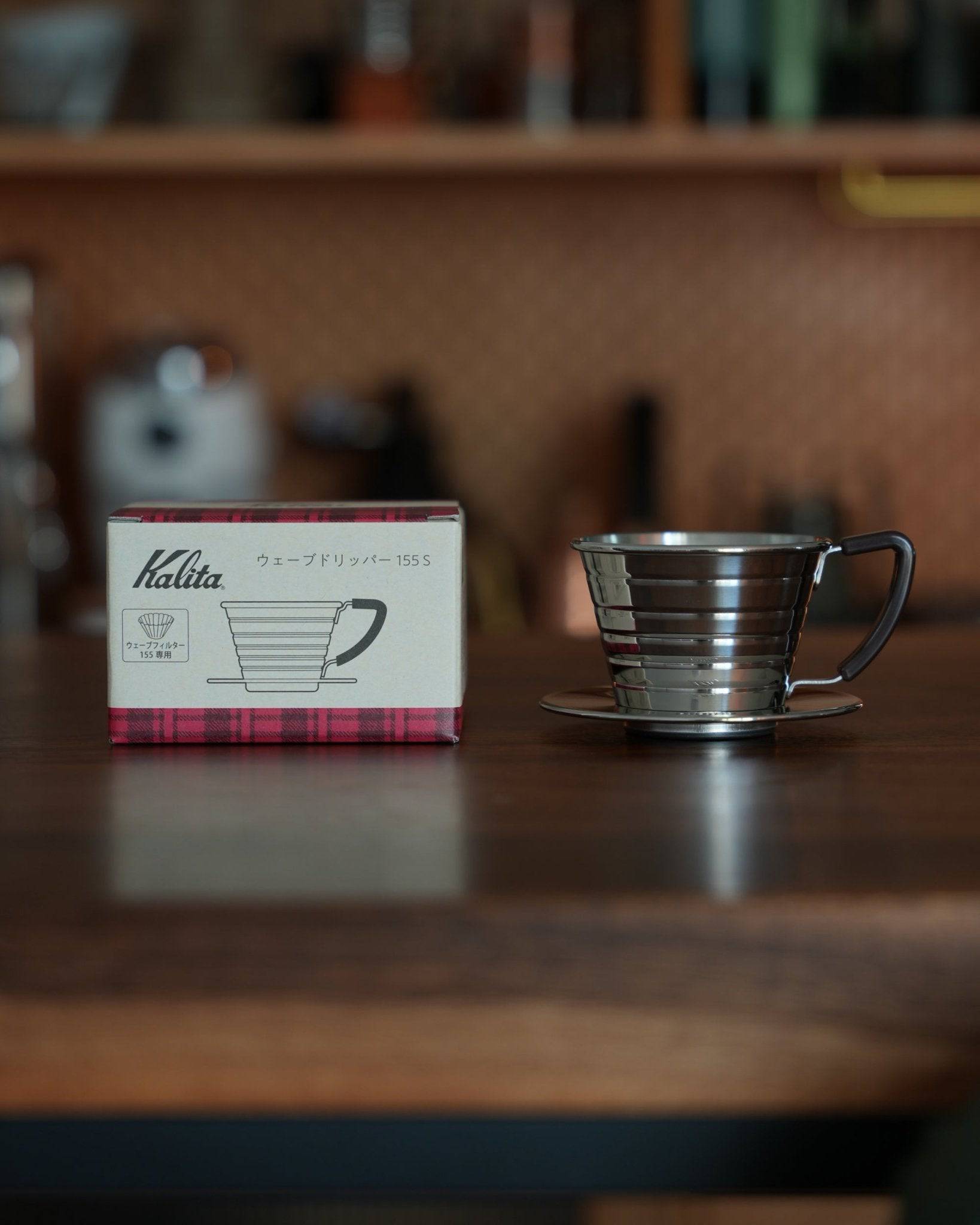Kalita Wave 155 S stainless steel coffee dripper with box on wooden table, showcasing its unique wave pattern design for optimal coffee extraction