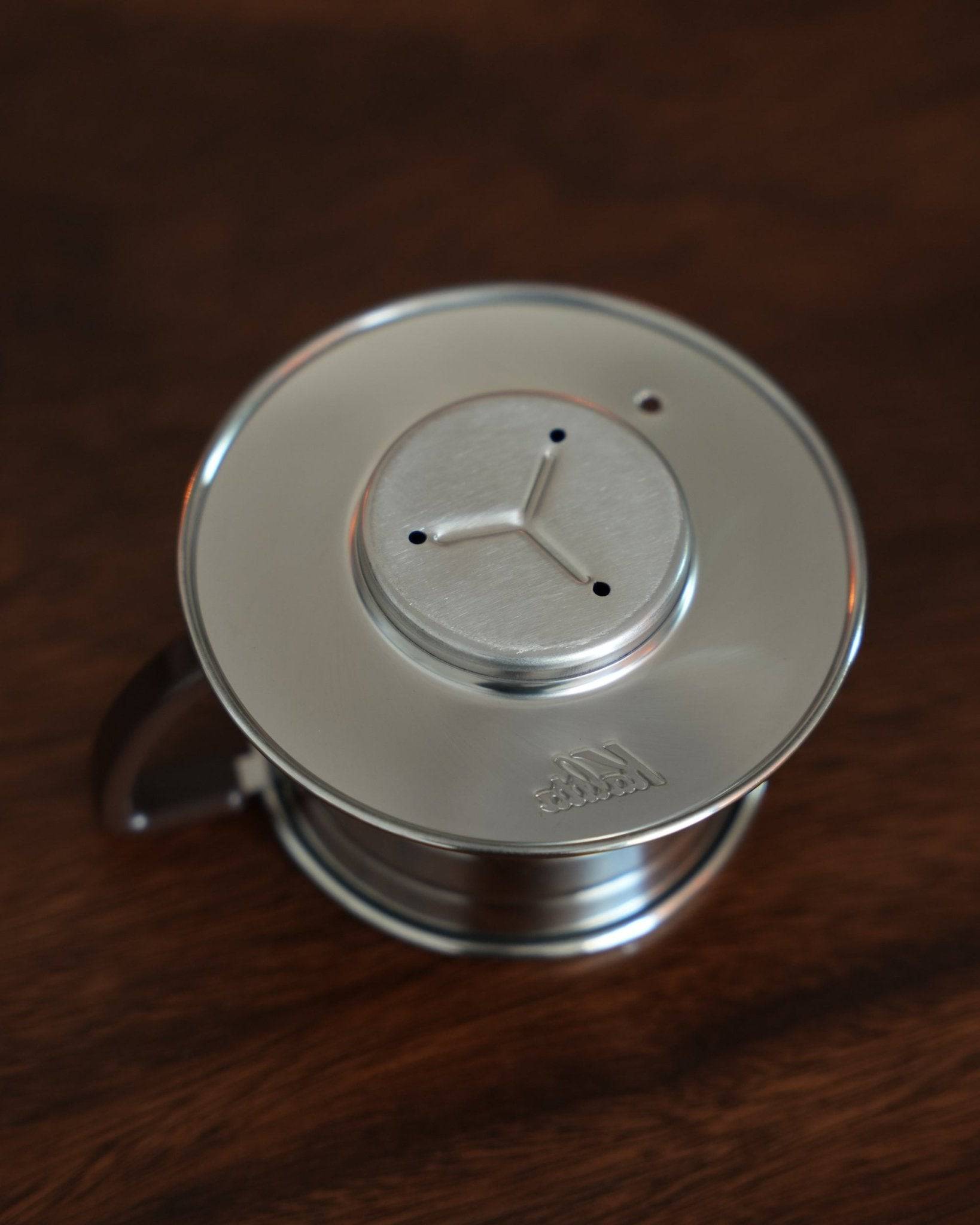 Kalita Wave 155 S stainless steel coffee dripper with three-hole design on wooden surface, showcasing its unique wave pattern and premium build quality for optimal coffee extraction
