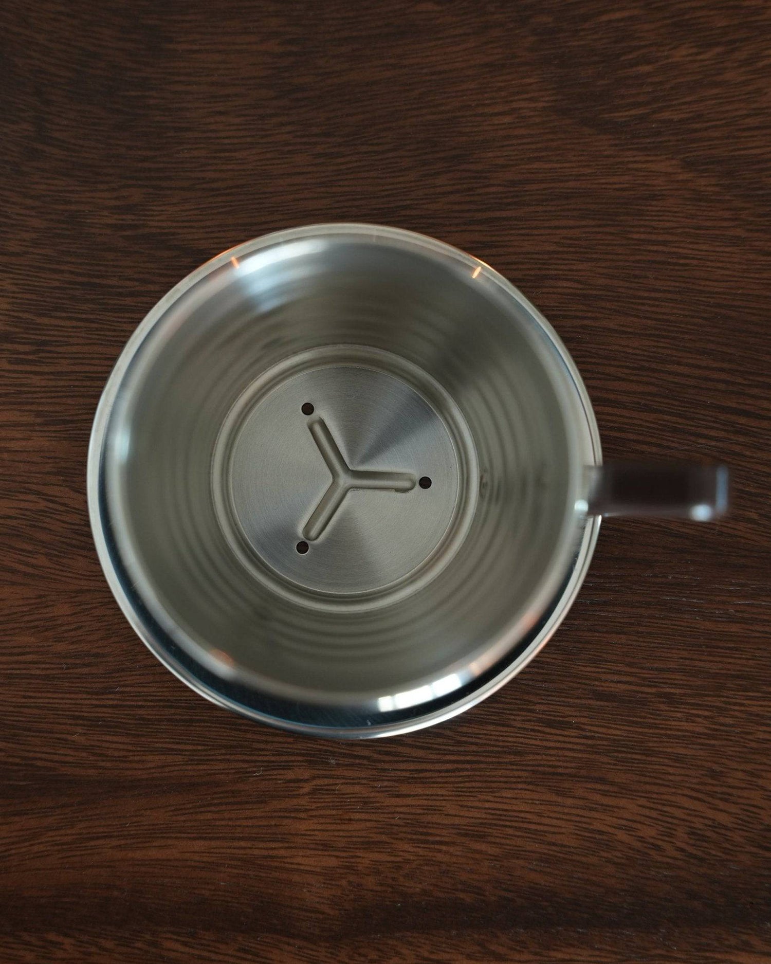 Kalita Wave 155 S stainless steel pour-over coffee dripper with unique wave pattern and three-hole design, seen from above on dark wooden surface, showcasing its durable construction and precision brewing features