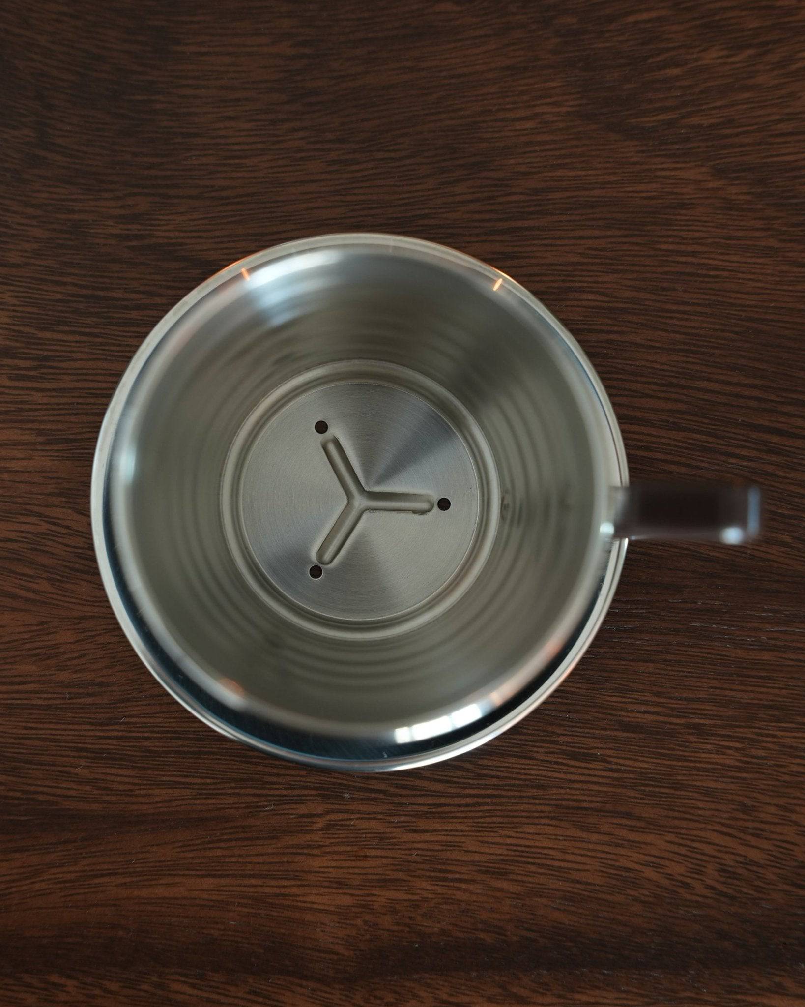 Kalita Wave 155 S stainless steel pour-over coffee dripper with unique wave pattern and three-hole design, seen from above on dark wooden surface, showcasing its durable construction and precision brewing features