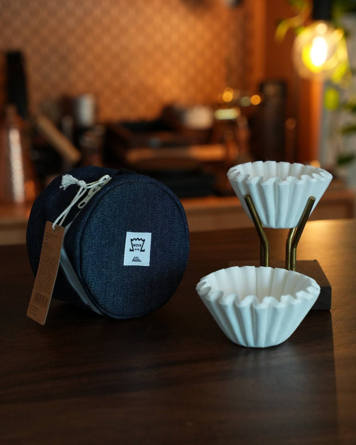 Kalita Wave coffee filter storage bag with white coffee filters on wooden table, warm cafe background