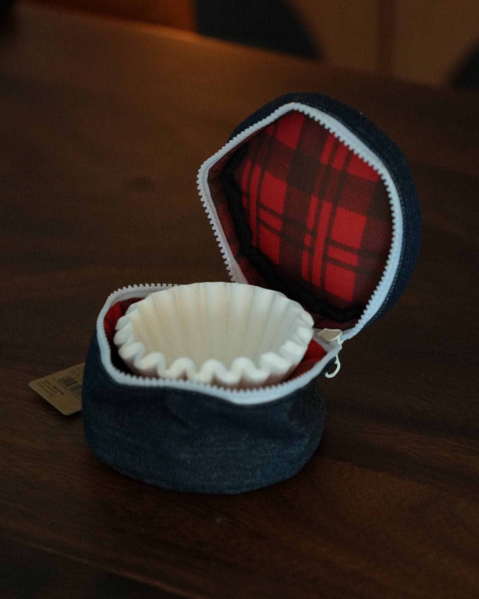 Kalita Wave coffee filter storage bag, open to reveal red plaid interior and white filter, sitting on wooden surface, showcasing compact design and protective functionality