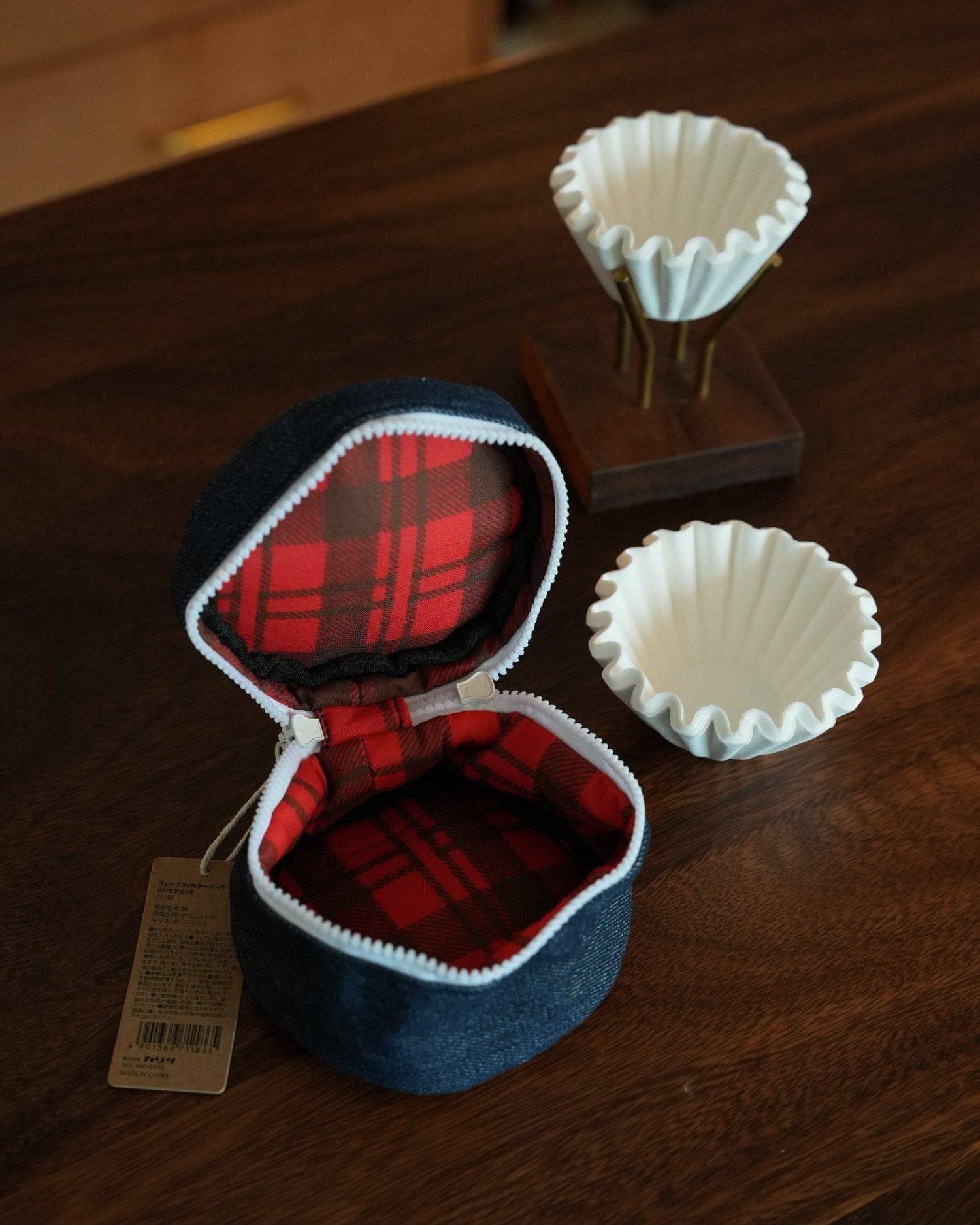 Kalita Wave coffee filter storage bag with red plaid interior, shown open next to white paper coffee filters on wooden surface