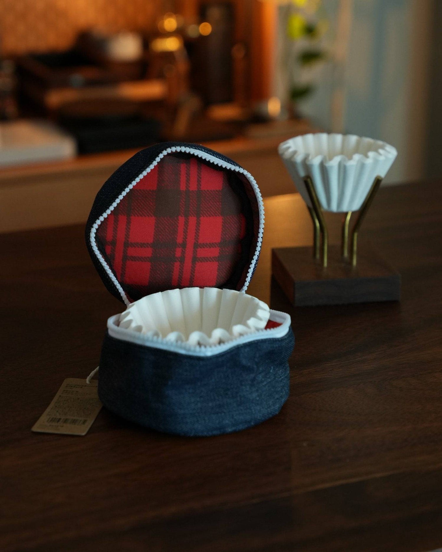 Stylish Kalita Wave coffee filter storage bag with red plaid interior, open to display white filter, next to decorative filter holder on wooden table in cozy setting
