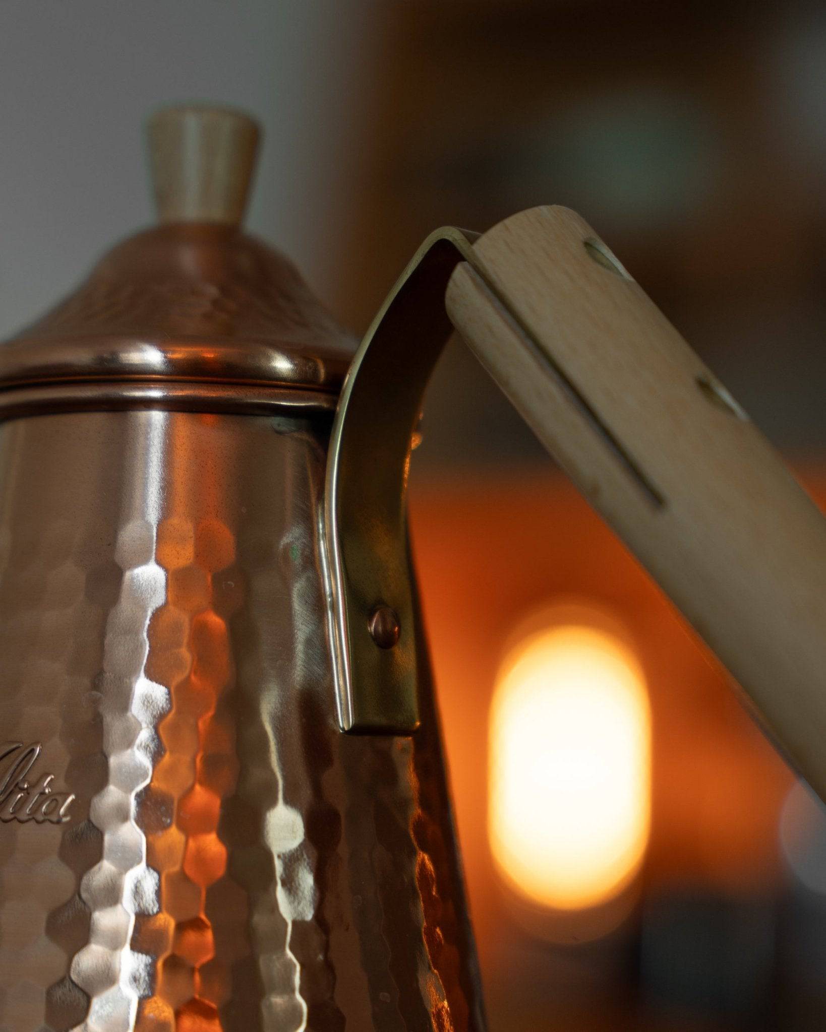Kalita x Tsubame copper pour-over kettle with wooden handle, featuring honeycomb pattern and gooseneck spout, illuminated by warm light, showcasing Japanese craftsmanship for precision coffee brewing