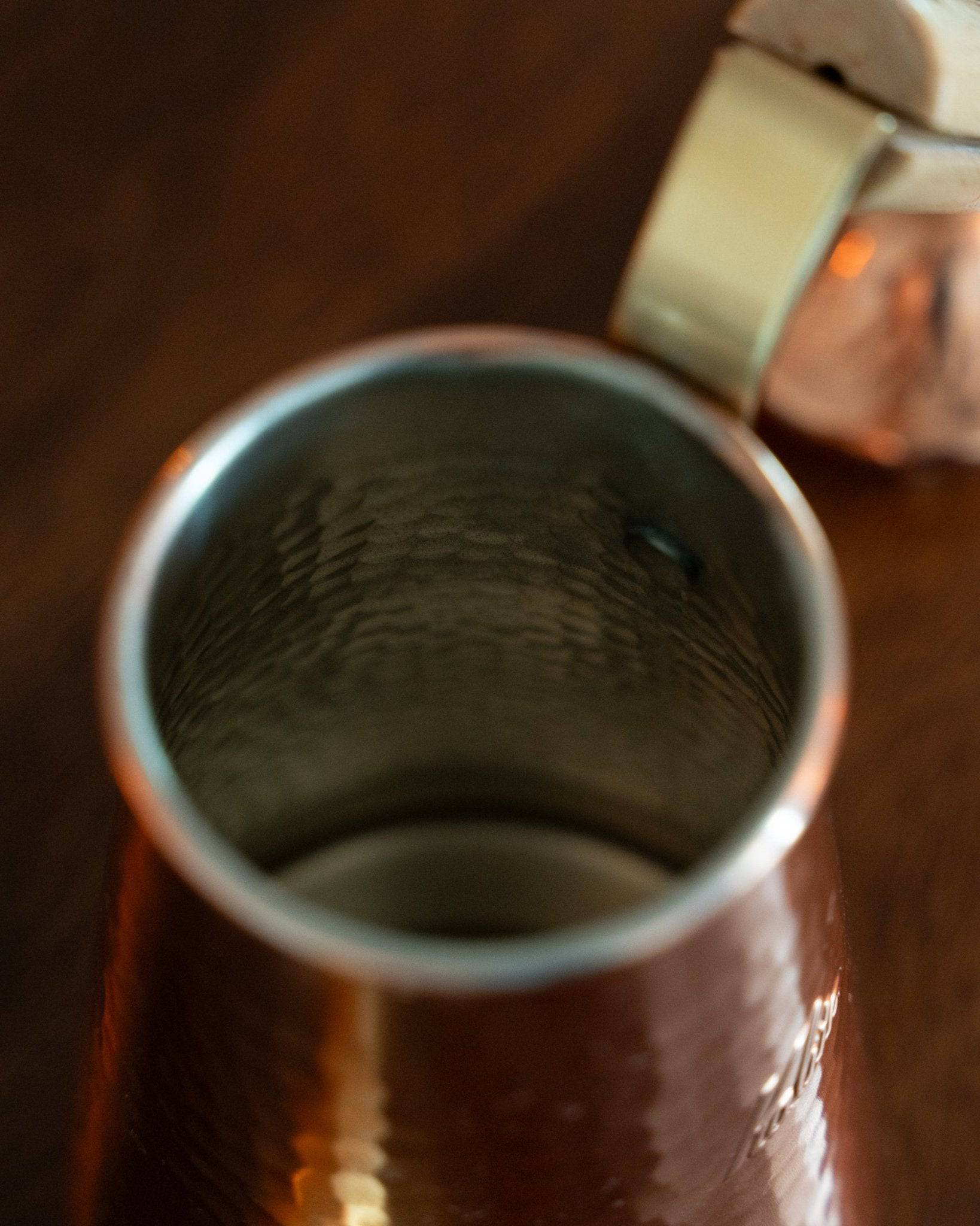 Close-up of Kalita x Tsubame copper pour-over kettle, showcasing its precision spout and interior craftsmanship. Copper body reflects warm light, highlighting the kettle&