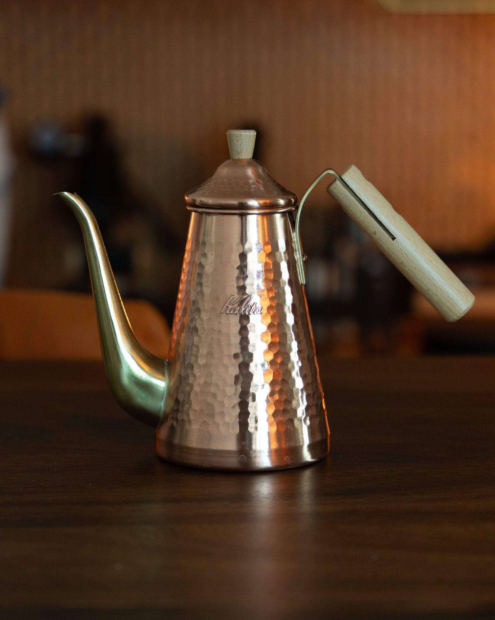 Kalita x Tsubame copper pour-over kettle with gooseneck spout and wooden handle, 700ml capacity, showcasing hammered texture and craftsmanship, positioned on wooden surface in warm lighting