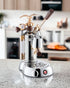 La Pavoni EXPO Lever Espresso Machine on kitchen counter, featuring gold eagle emblem, wooden handle, pressure gauge, and chrome finish. Luxurious design with vintage-inspired details and professional-grade components for crafting authentic Italian espresso.
