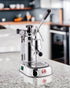 La Pavoni Professional Lusso lever espresso machine on kitchen counter, featuring chrome body, pressure gauge, steam wand, and manual lever for precise extraction control. Showcases Italian craftsmanship and traditional espresso-making experience.