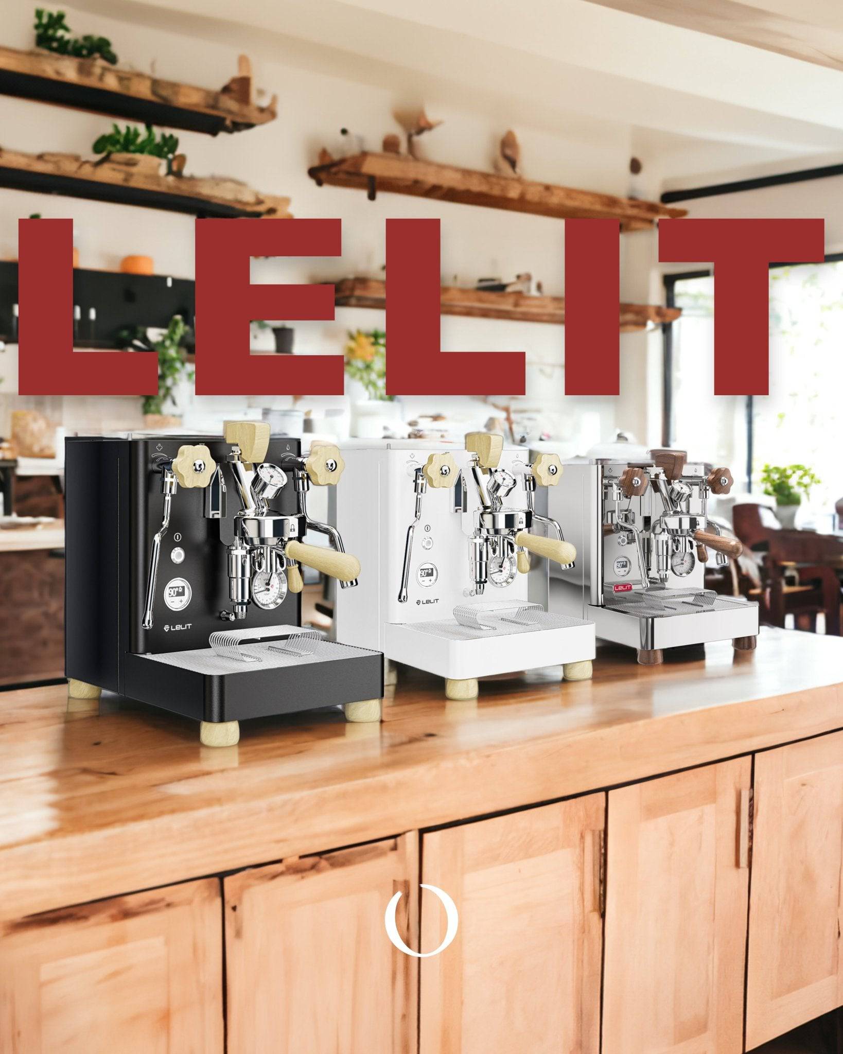 Three Lelit espresso machines in black, white, and silver on a wooden counter in a modern coffee shop, with the Lelit logo prominently displayed above them.
