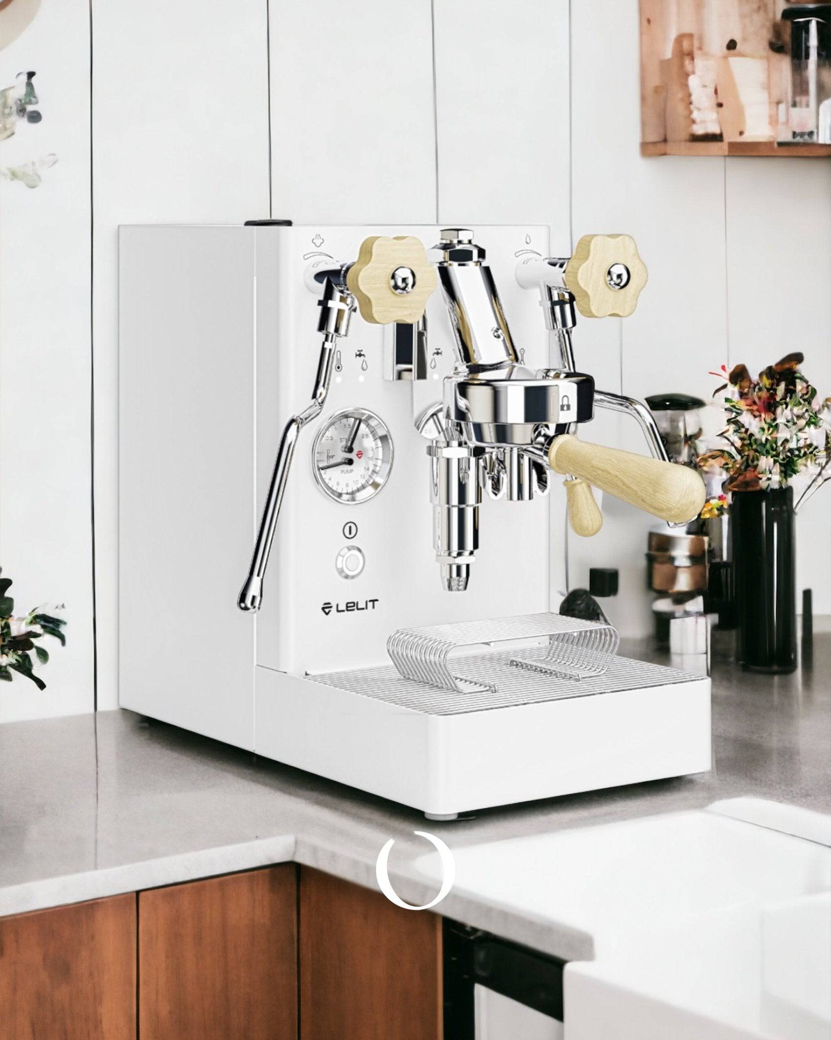 Lelit MaraX V2 PL62X espresso machine with white body and gold accents on kitchen countertop, featuring pressure gauge and steam wand, surrounded by coffee accessories and plants