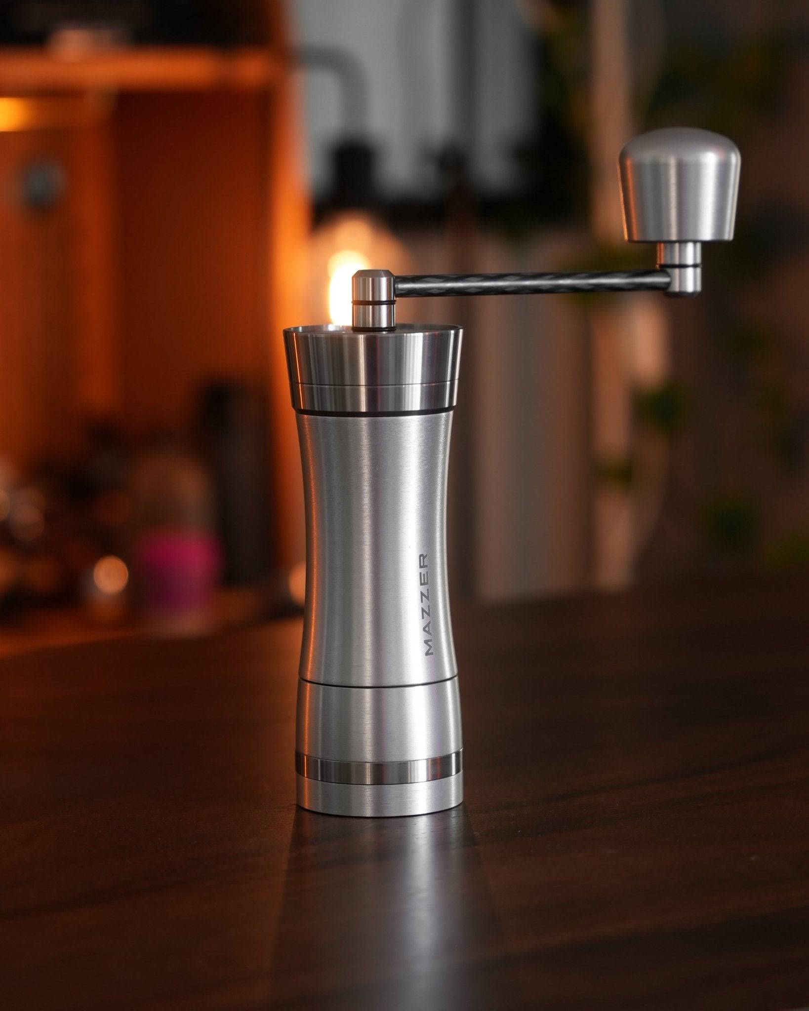 Mazzer Omega Soft manual coffee grinder on wooden table, stainless steel body with adjustable grind settings, ergonomic handle, compact design for home and travel use, professional-grade conical burrs for consistent grind quality