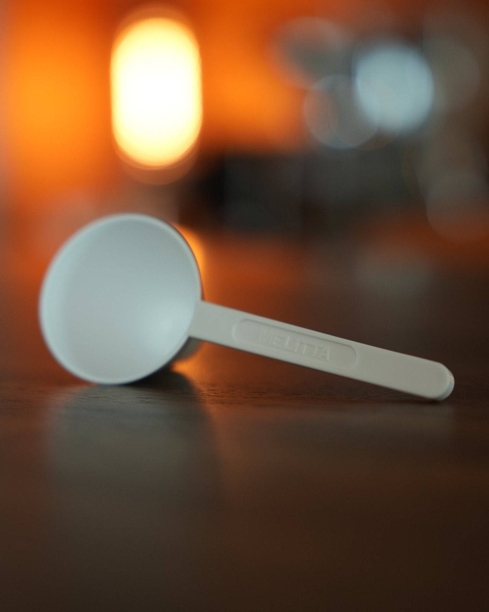 Melitta coffee measuring scoop on wooden surface with warm, blurred background lighting, showcasing premium quality and attention to detail in coffee accessories