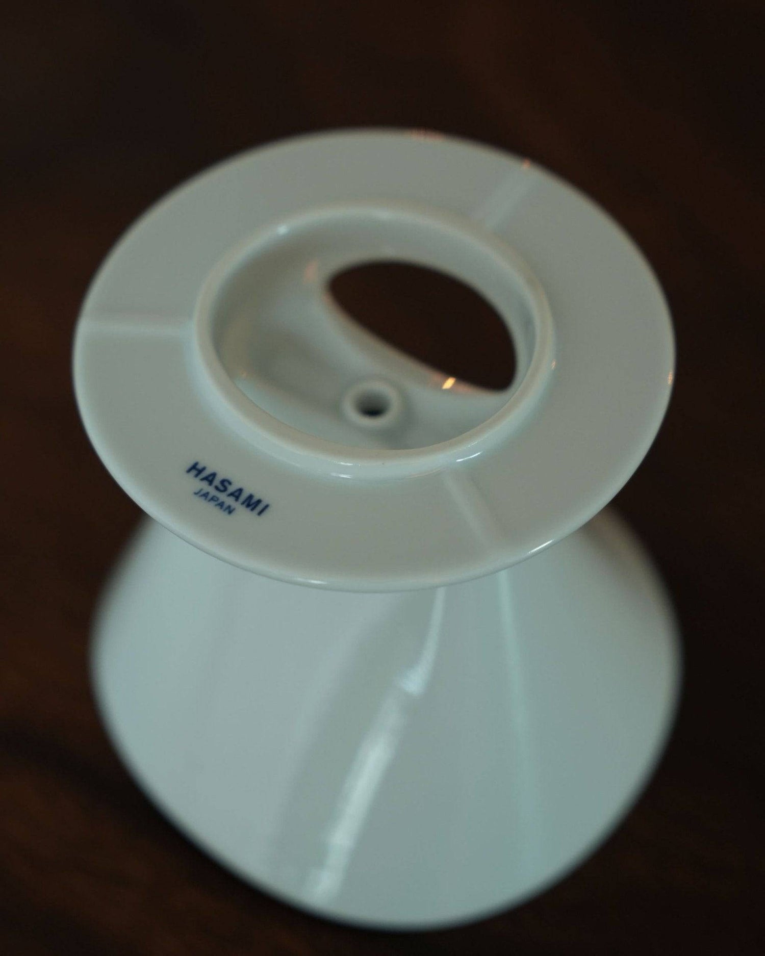 White ceramic Melitta and HASAMI coffee dripper with unique single-hole design, featuring ribbed interior and asymmetrical shape, showcasing Hasami-yaki craftsmanship on a dark background