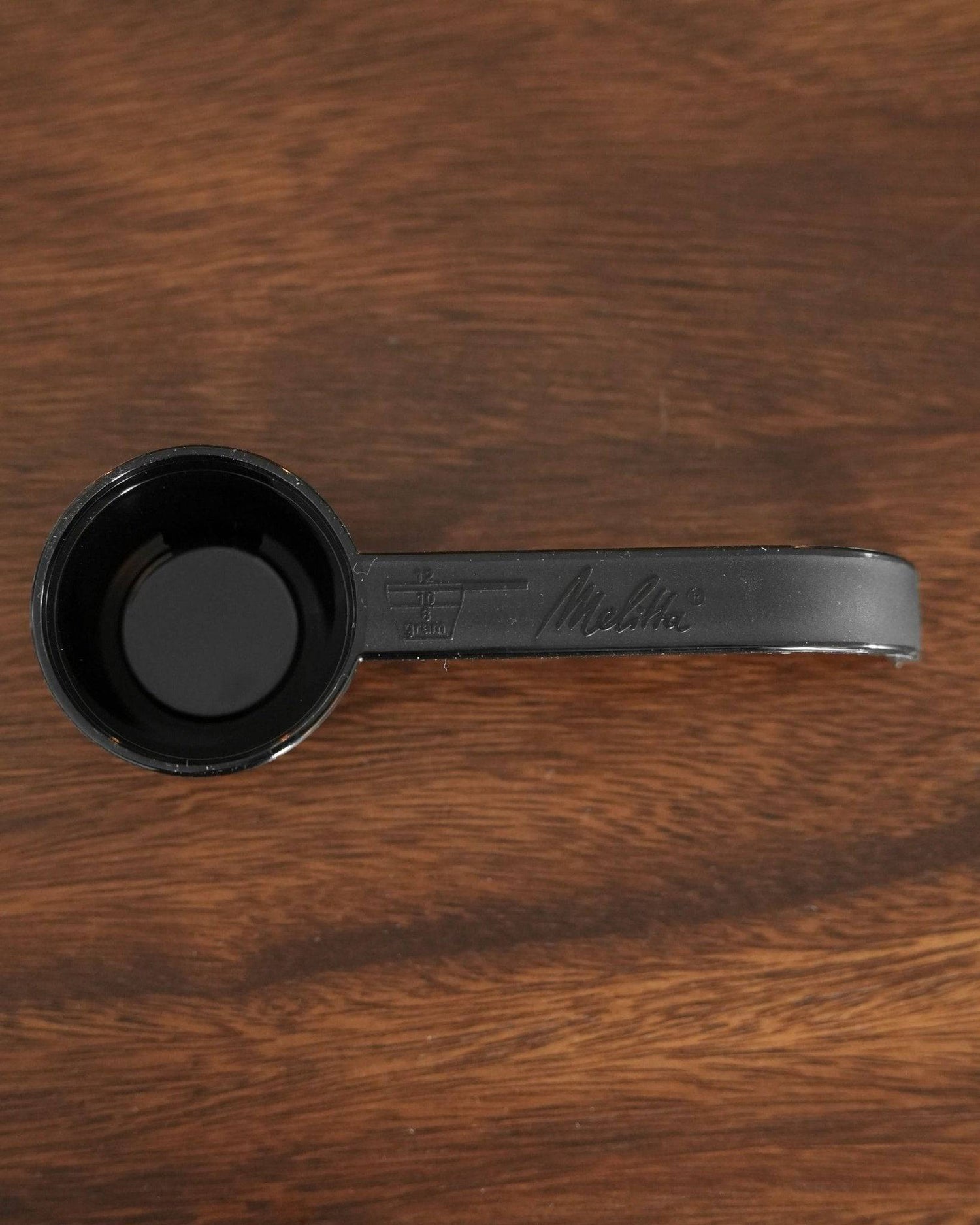 Black Melitta coffee scoop on wooden background, featuring measuring markings and brand logo embossed on handle