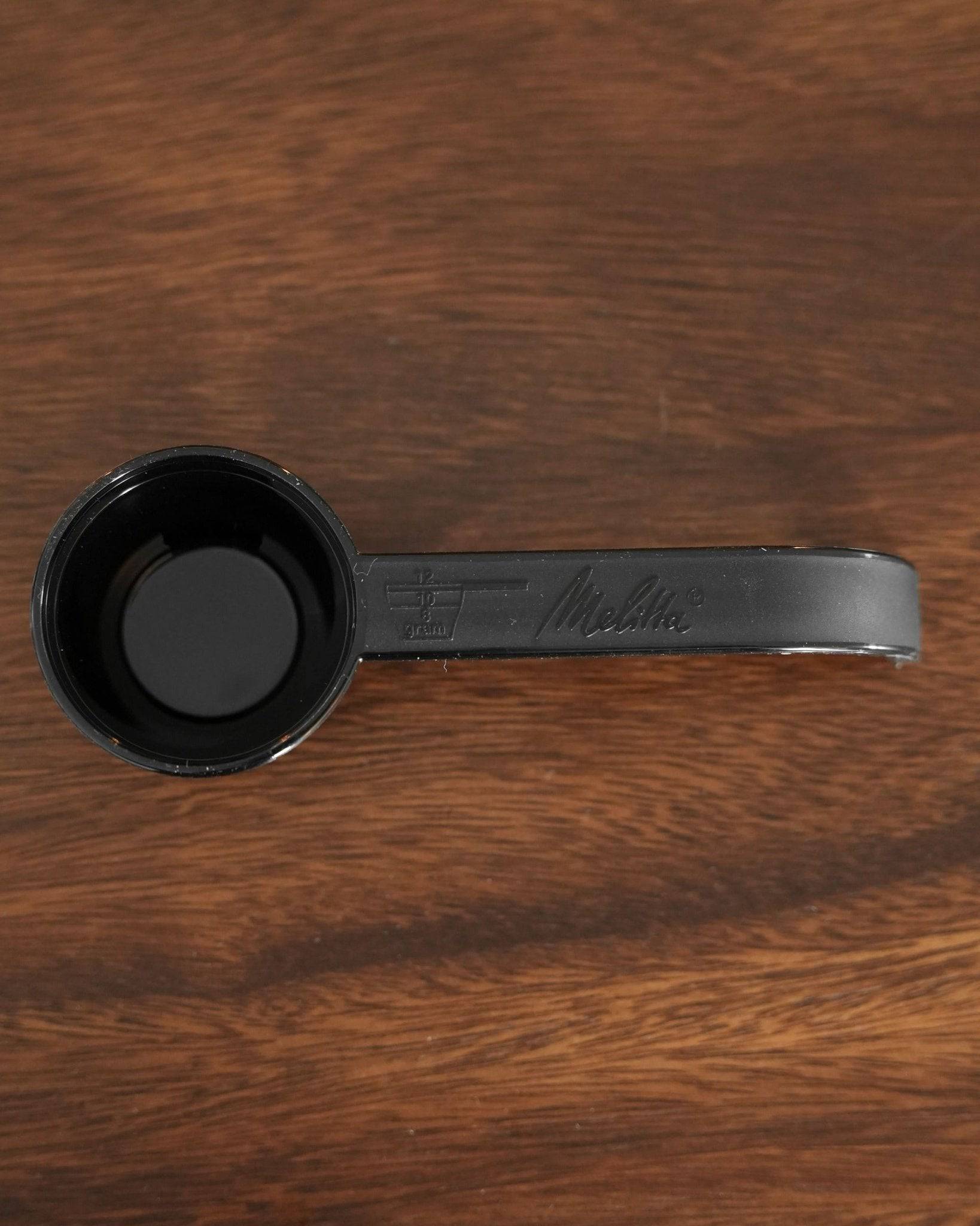Black Melitta coffee scoop on wooden background, featuring measuring markings and brand logo embossed on handle