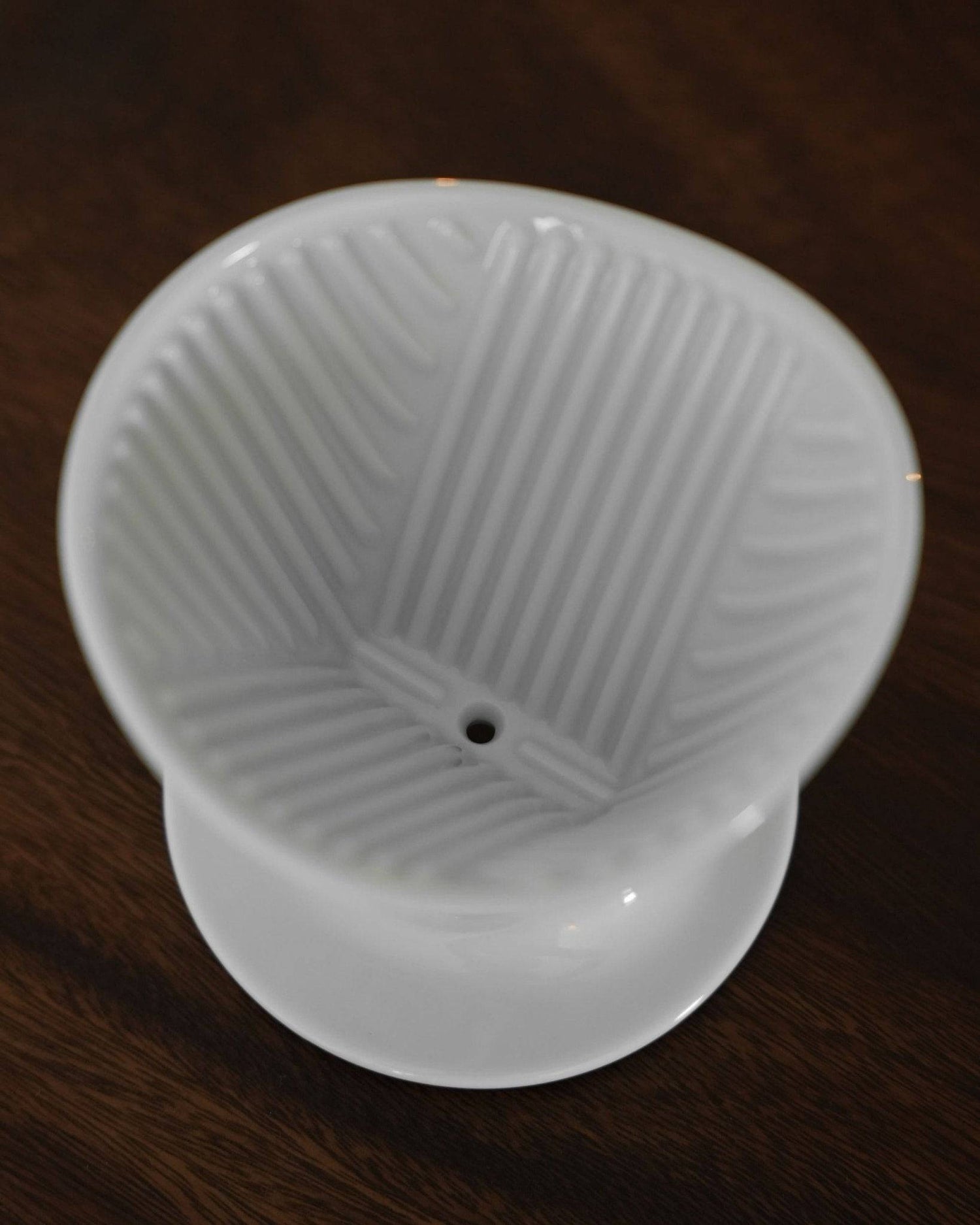 Melitta & HASAMI ceramic pour-over coffee dripper with ribbed interior, single-hole design, and unique asymmetrical shape on wooden surface, showcasing Japanese Hasami-yaki craftsmanship