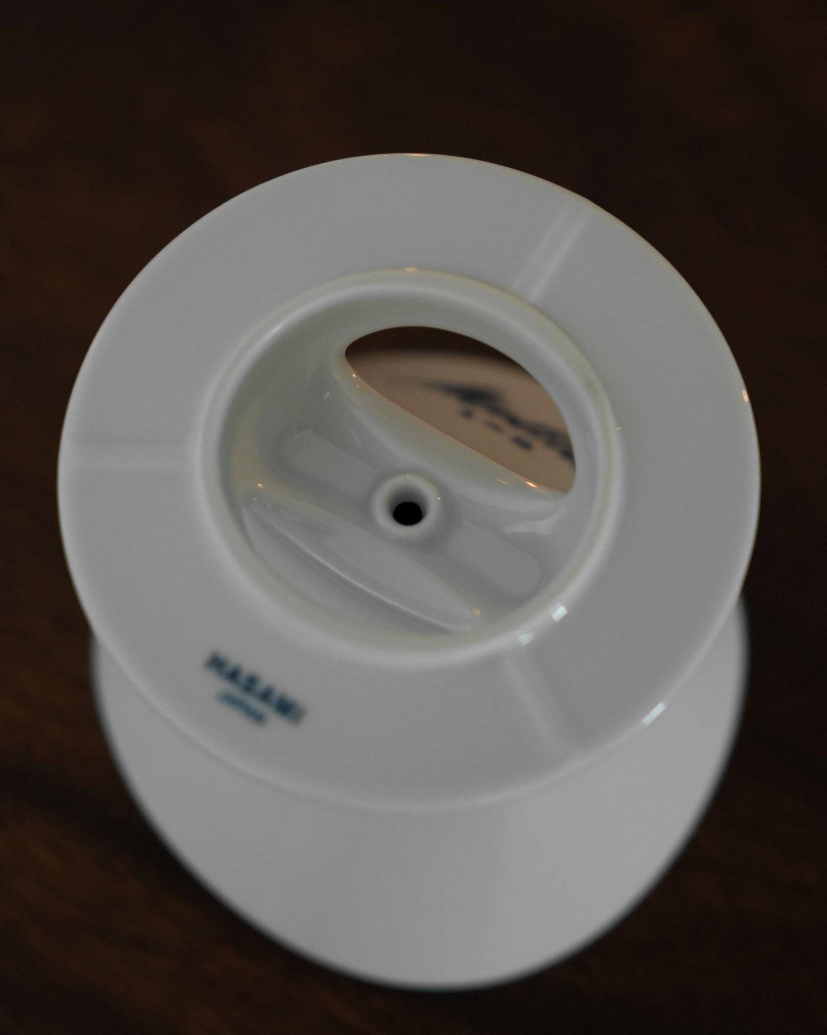 White ceramic Melitta coffee dripper with single hole design, ribbed interior, and blue logo, positioned on a white ceramic base plate, showcasing Japanese Hasami porcelain craftsmanship