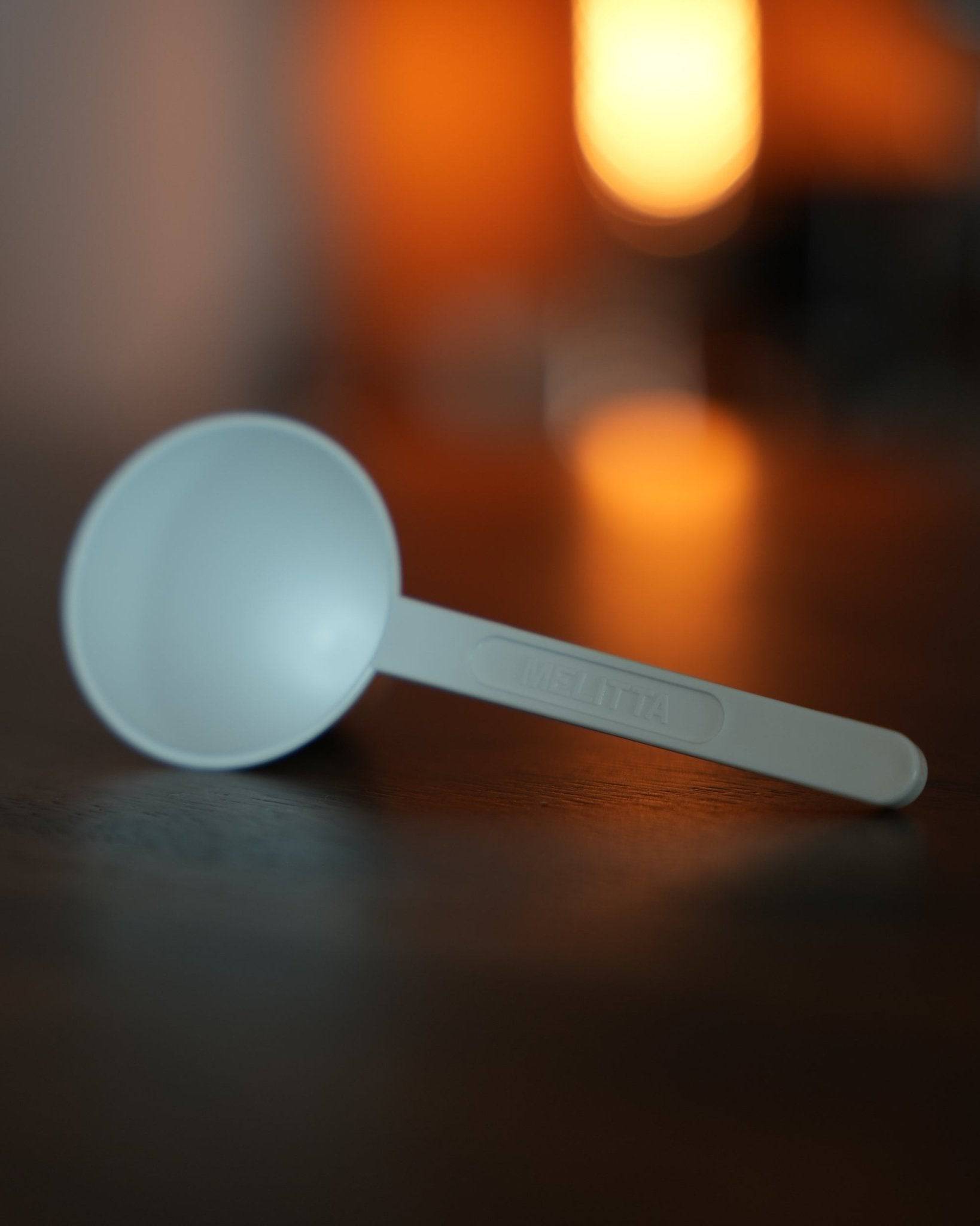 Melitta turquoise blue coffee scoop on wooden surface with warm, blurred background lighting, showcasing the product&