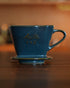 Melitta turquoise blue pour-over coffee dripper with gold lettering, placed on wooden surface, showcasing elegant design and premium craftsmanship of Japanese Mino-yaki pottery