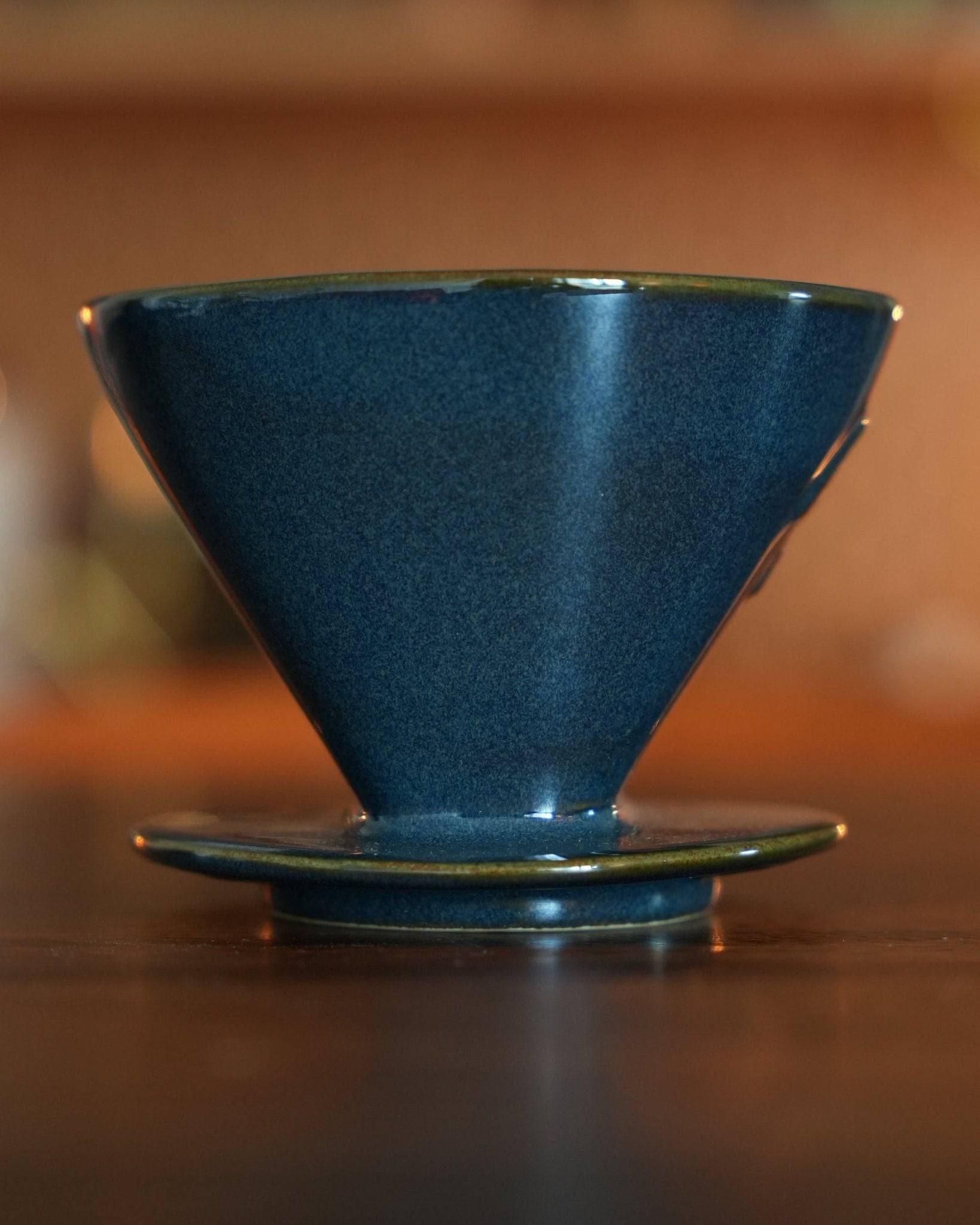 Melitta turquoise blue coffee dripper on wooden surface, showcasing its conical shape and glossy ceramic finish, perfect for brewing artisanal coffee