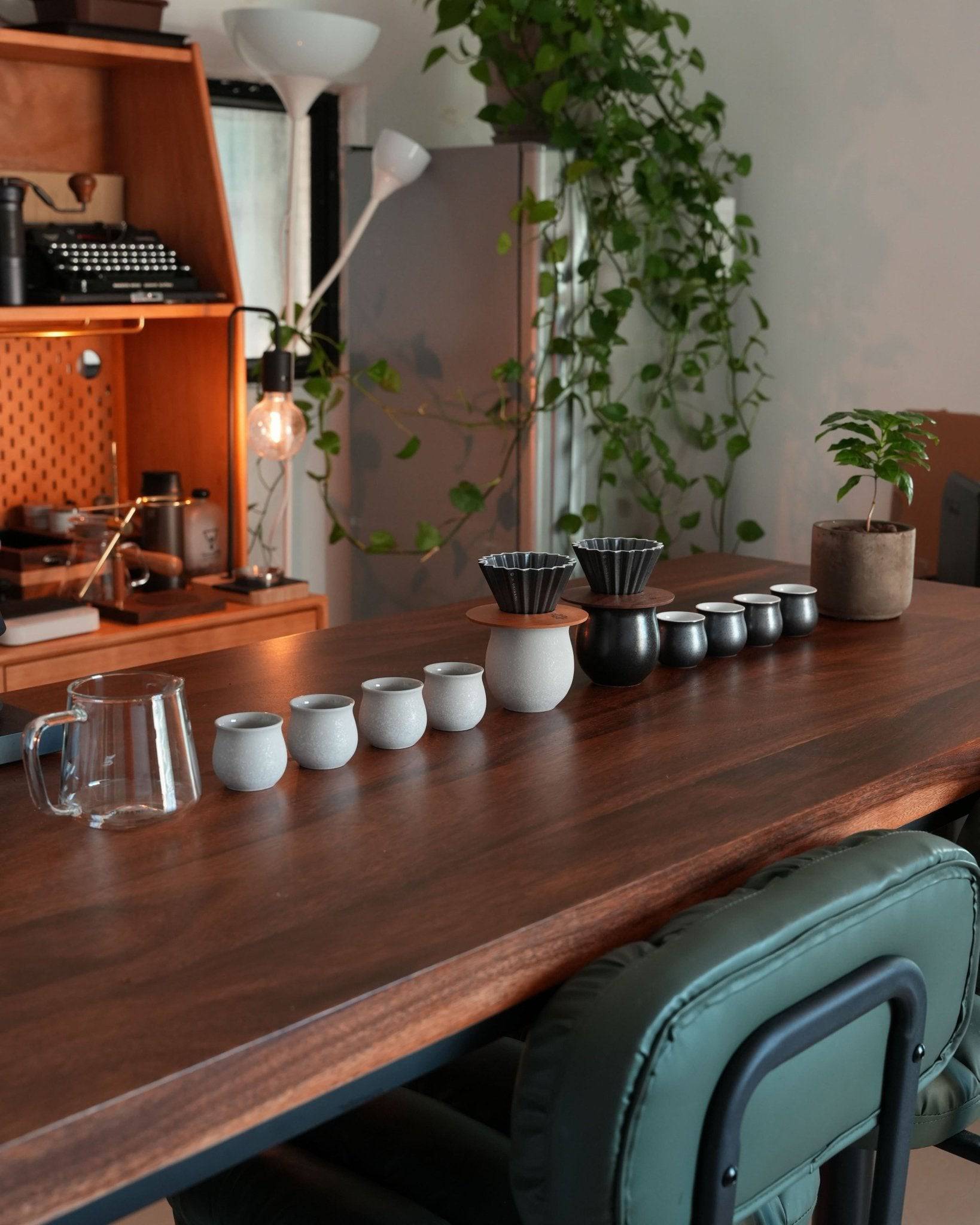 Ninety Plus pour-over coffee set displayed on wooden table with vintage decor, including typewriter and plants, showcasing elegant cups, filters, and brewing equipment for a premium coffee experience
