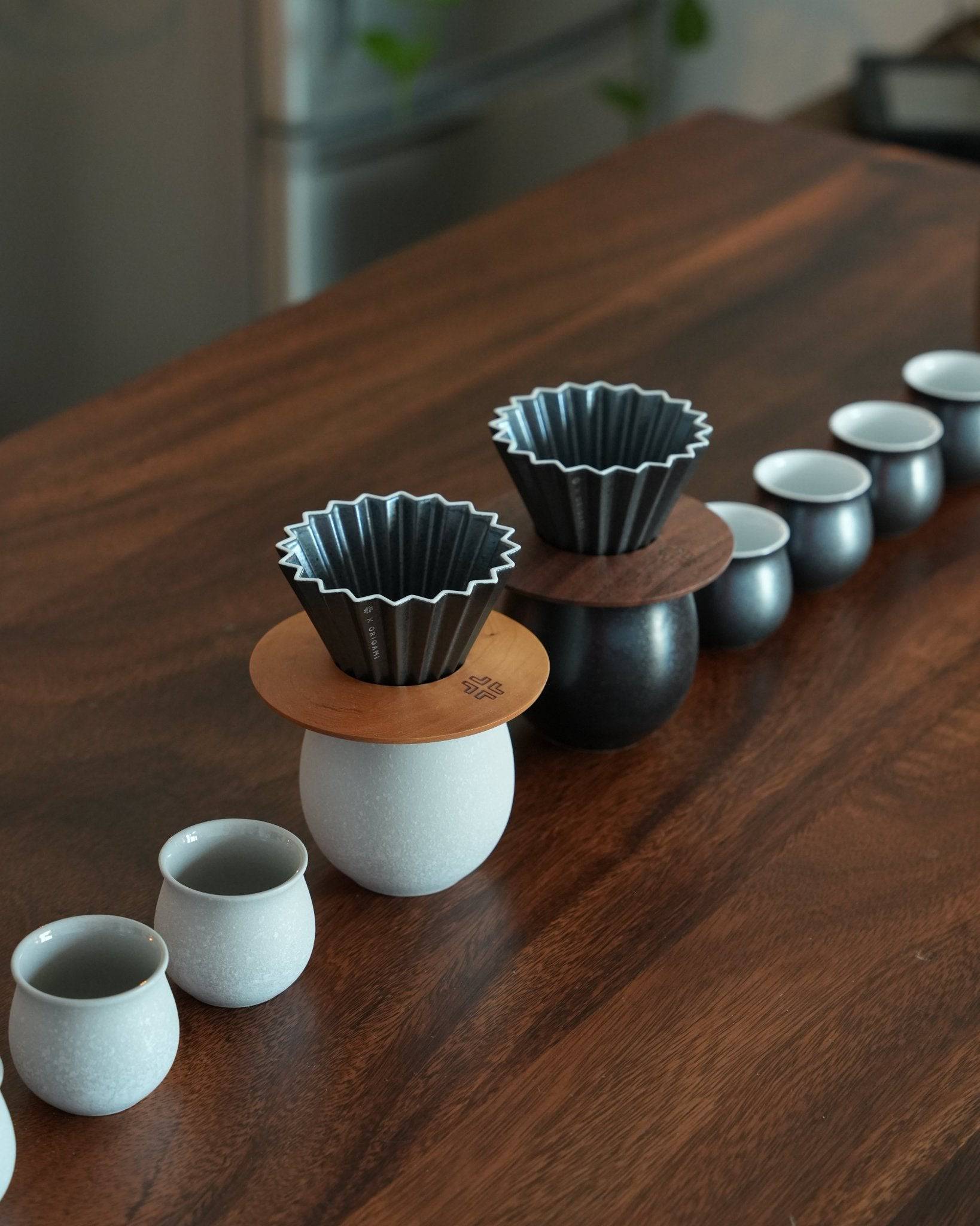 Ninety Plus pour-over coffee set featuring ceramic cups, wooden holders, and metal filters arranged on a dark wooden table, showcasing modern minimalist design for artisanal coffee brewing
