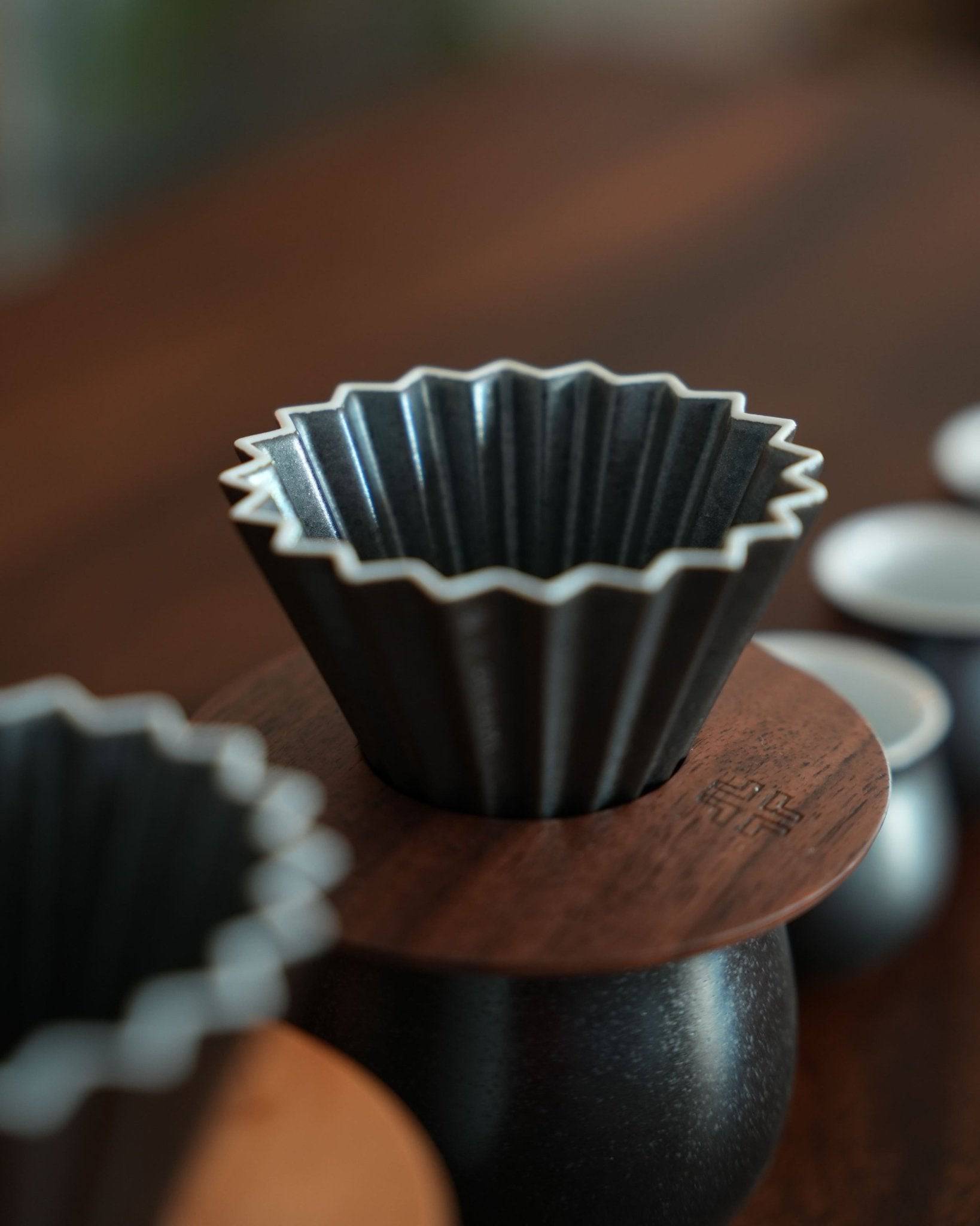 Close-up of a black fluted coffee filter on a wooden surface, part of the Ninety Plus pour-over coffee brewing set in Basalt white, showcasing its premium design and quality craftsmanship for coffee enthusiasts.