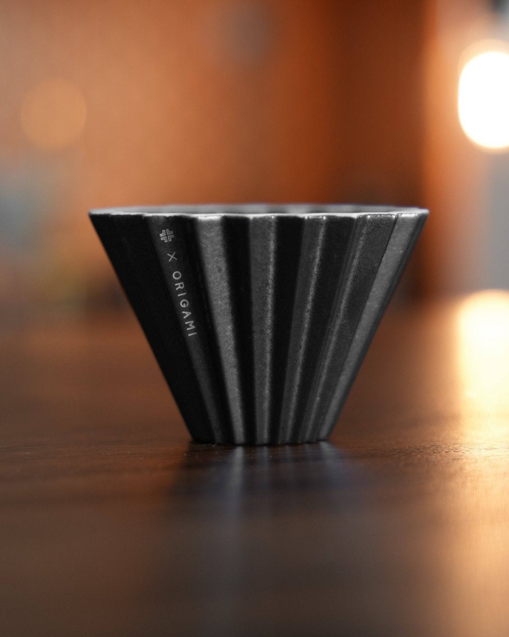 Ninety Plus Coffee Kone 10.1 mini brewing dripper, black obsidian color, conical shape with ribbed design, on wooden surface with soft warm background lighting