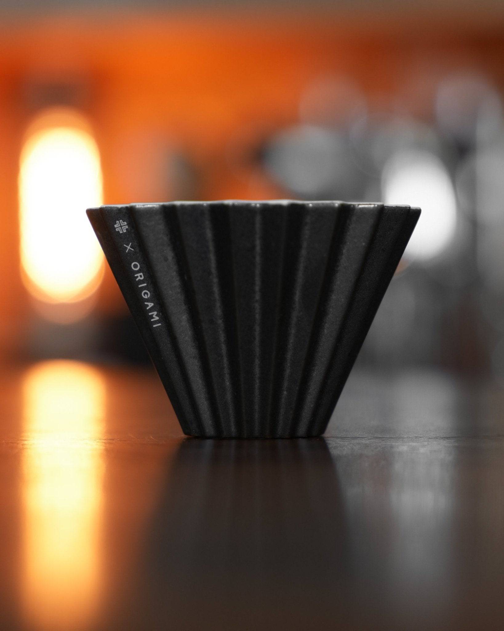 Ninety Plus Coffee Kone 10.1 mini brew dripper, black obsidian color, conical shape with ridged exterior, designed for 10g coffee, warm lighting background, reflective surface