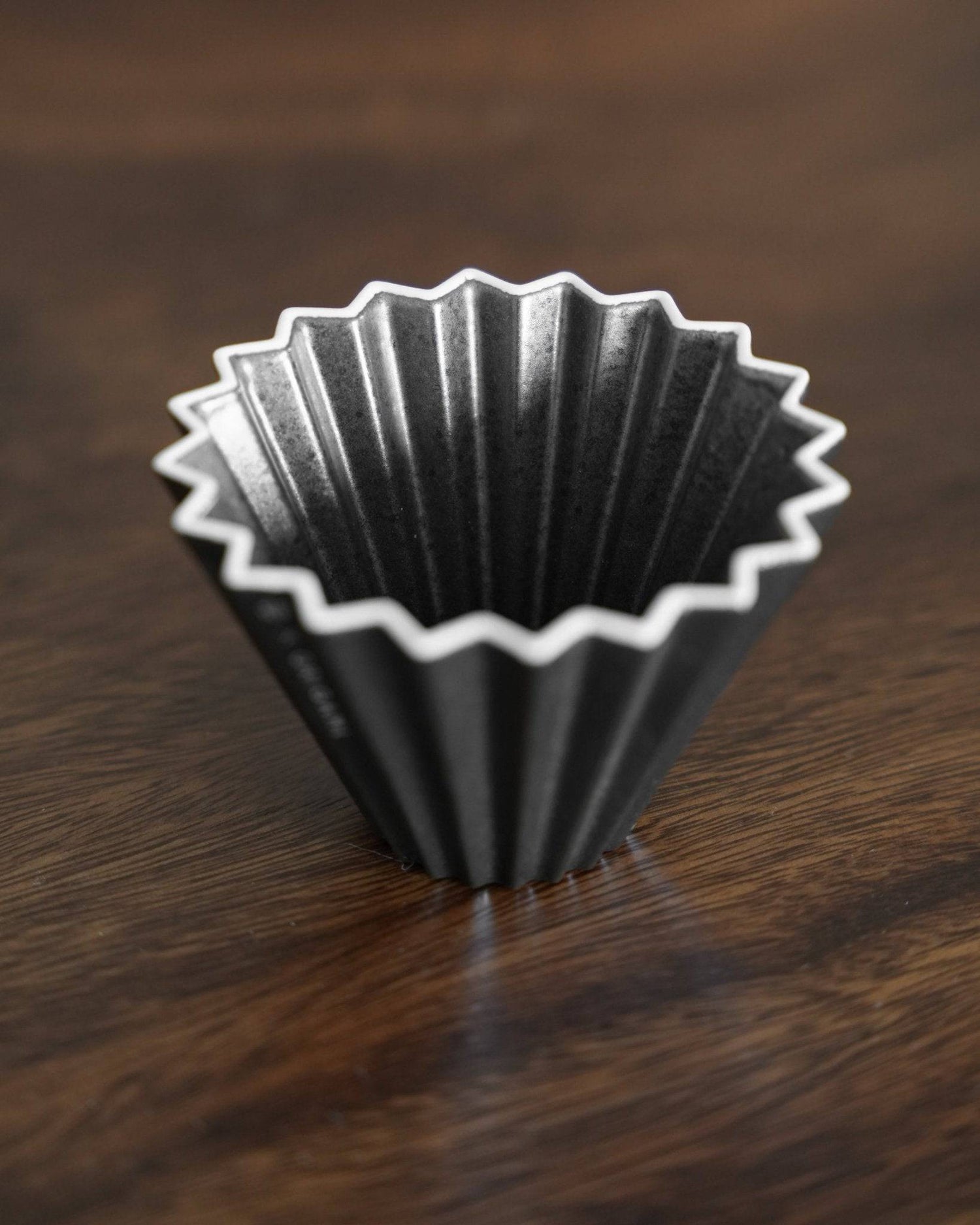 Ninety Plus Coffee Kone 10.1 mini coffee dripper with unique black obsidian color and pleated design, inspired by volcanic soil, sitting on a wooden surface for premium coffee brewing